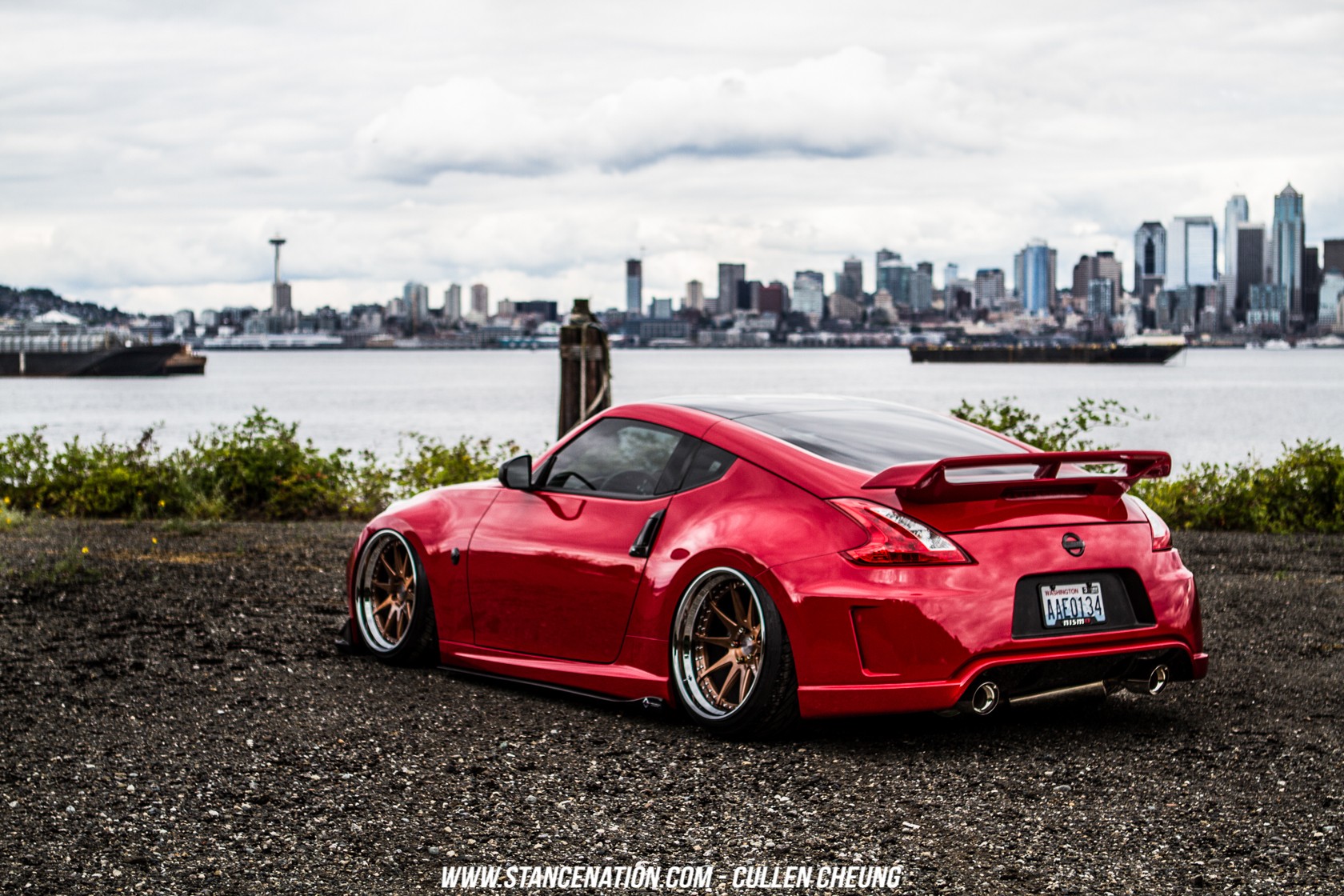 Red Nissan 370Z parked by the water with city skyline HD Wallpaper