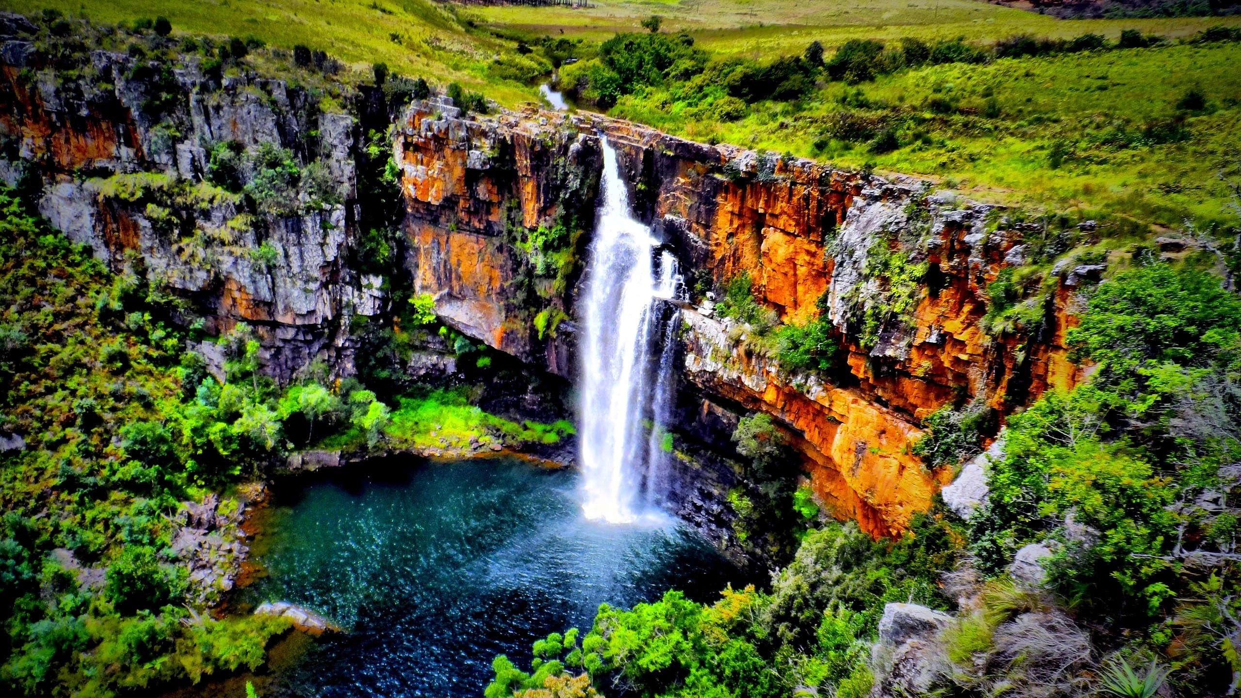 Waterfall cascading into a pool surrounded by cliffs and greenery HD Wallpaper