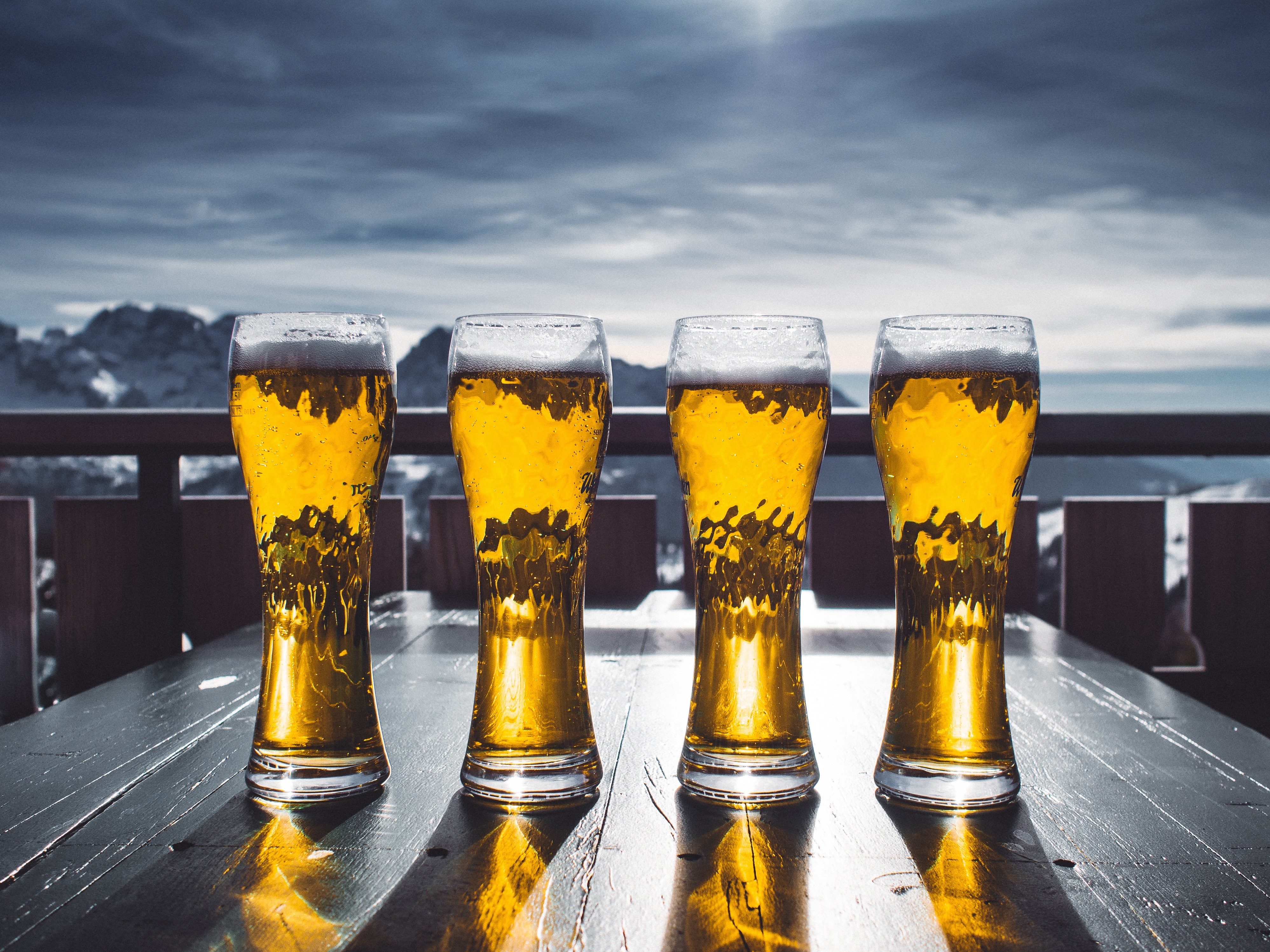 Four glasses of beer on a table with mountains in the background HD Wallpaper