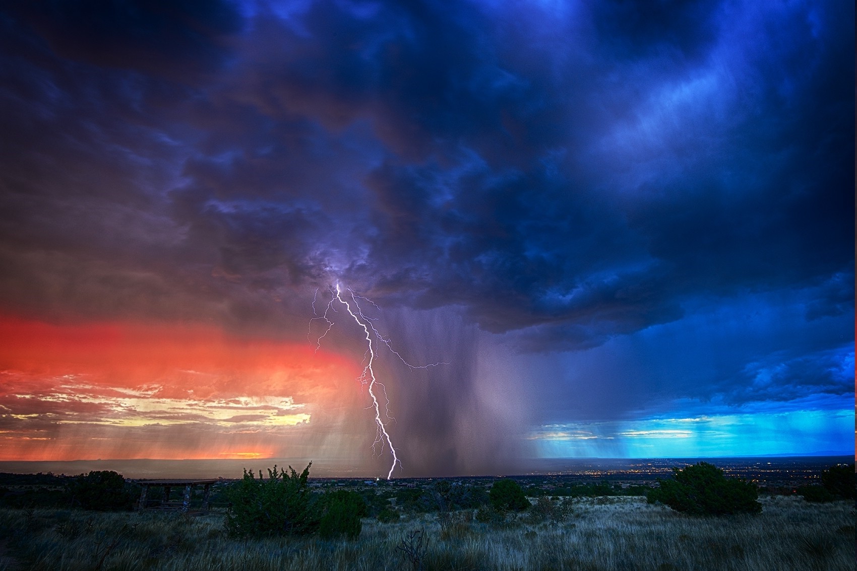 Lightning strikes during a colorful sunset storm over a landscape HD Wallpaper