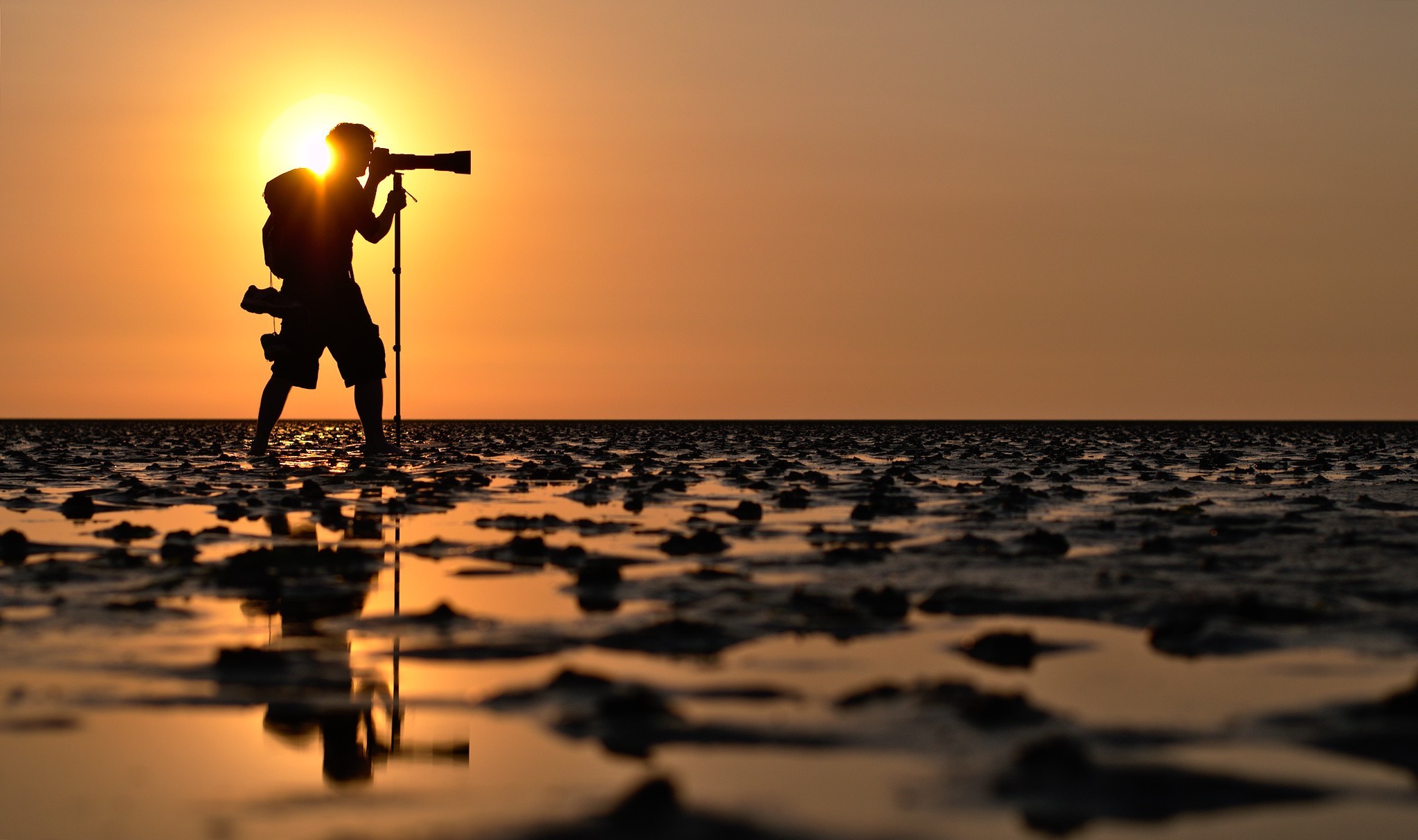 Photographer silhouetted against sunset on a beach HD Wallpaper