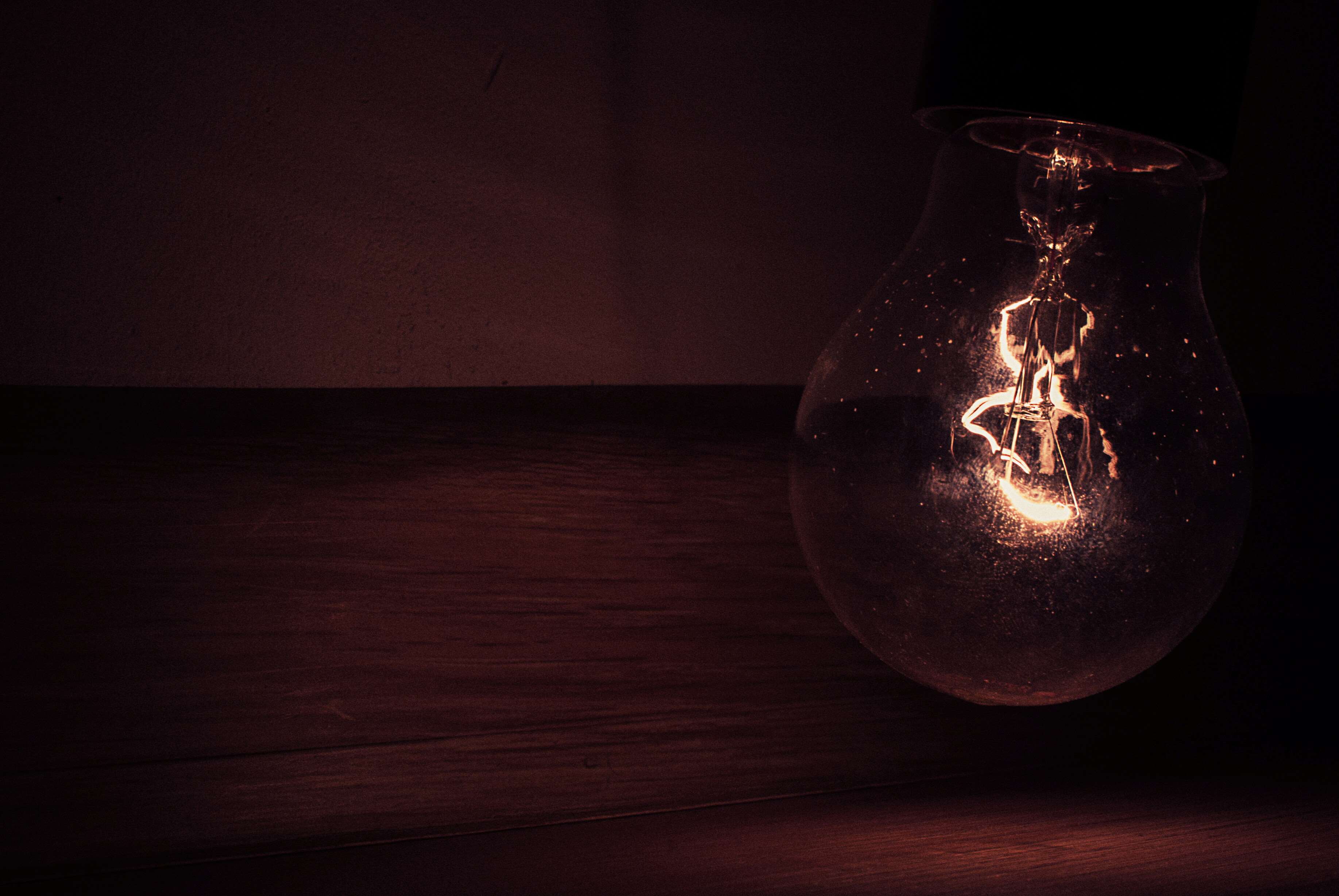 Close-up of a glowing light bulb on a wooden surface HD Wallpaper