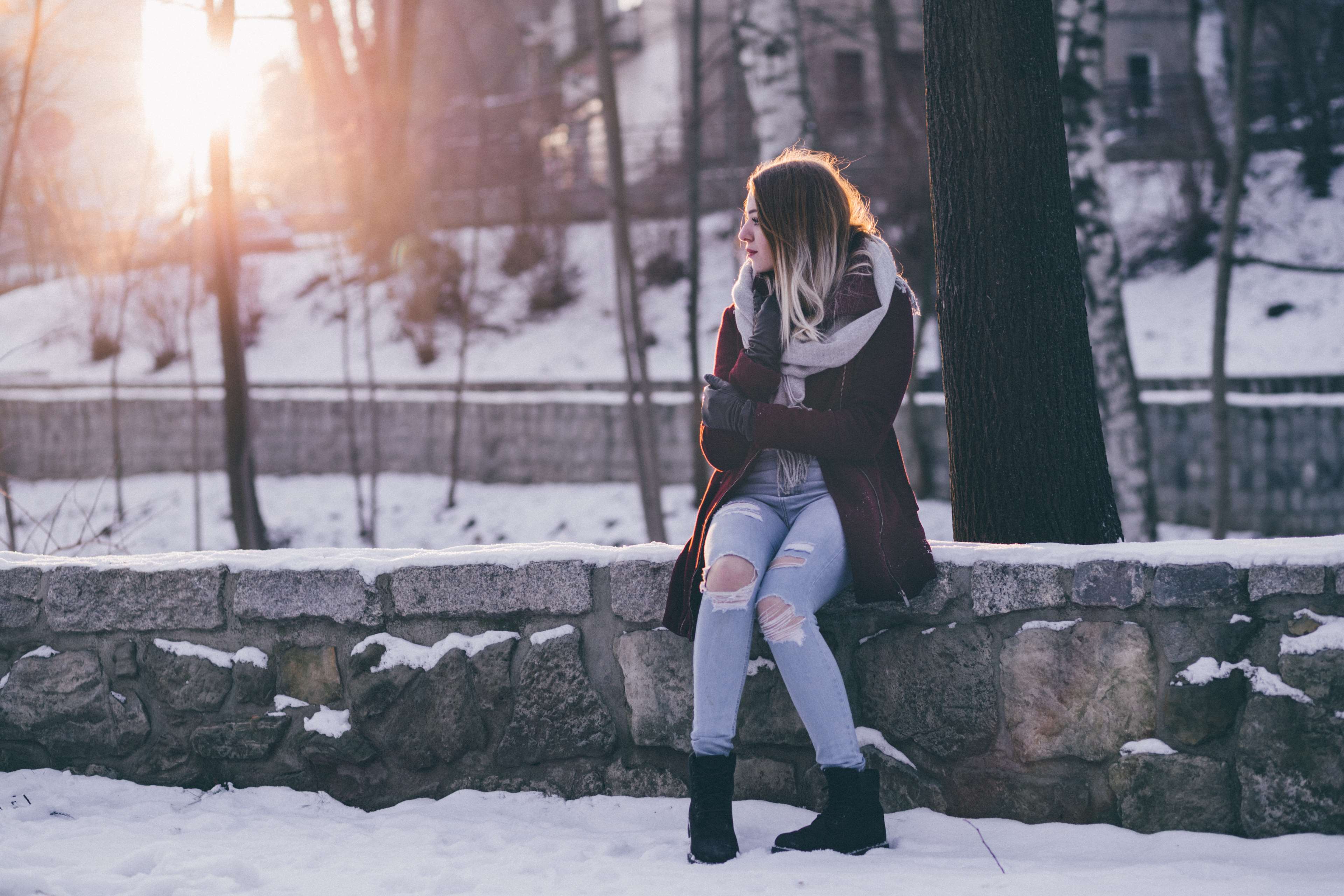 Woman in winter coat and ripped jeans sitting on a snowy wall HD Wallpaper