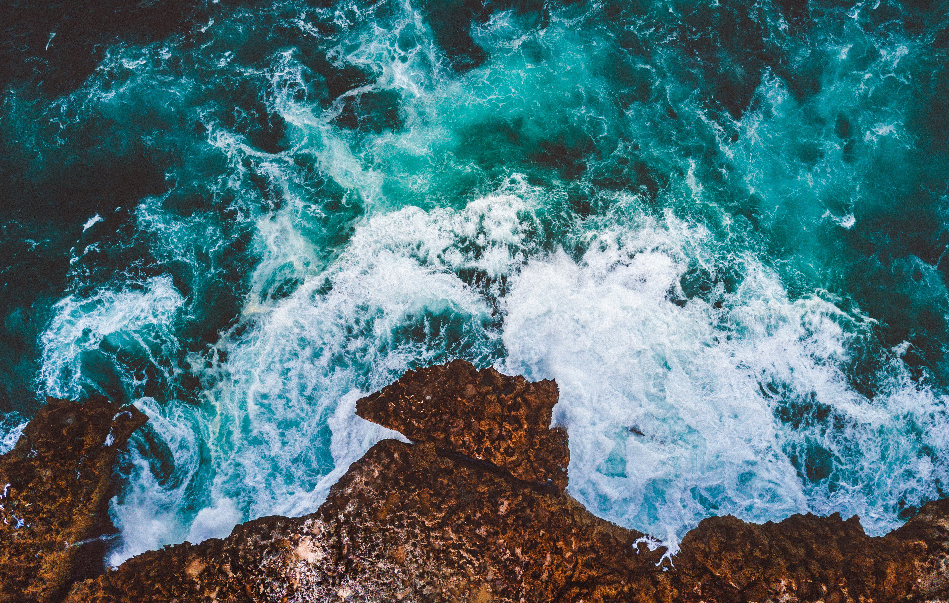 Aerial view of ocean waves crashing on a rocky cliff HD Wallpaper