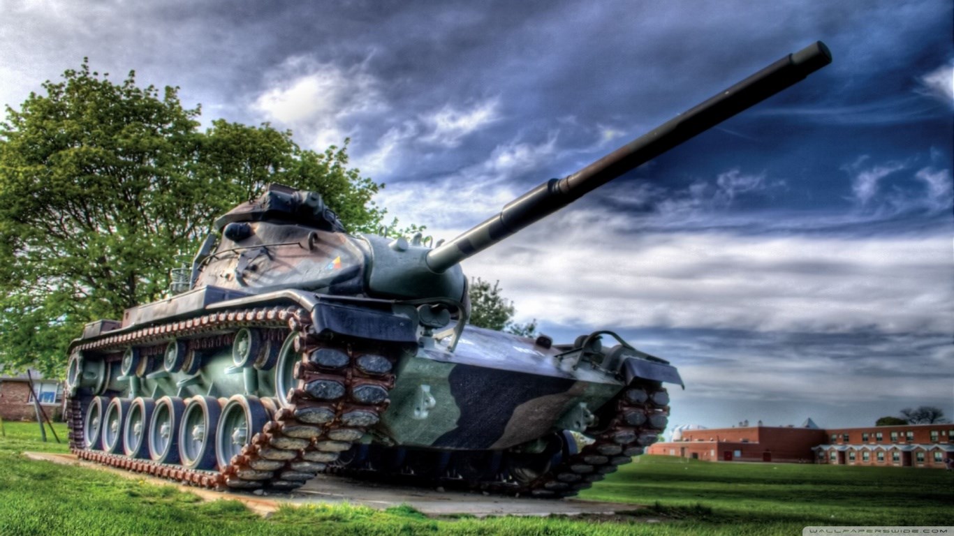 Tank in a grassy field with trees and buildings HD Wallpaper