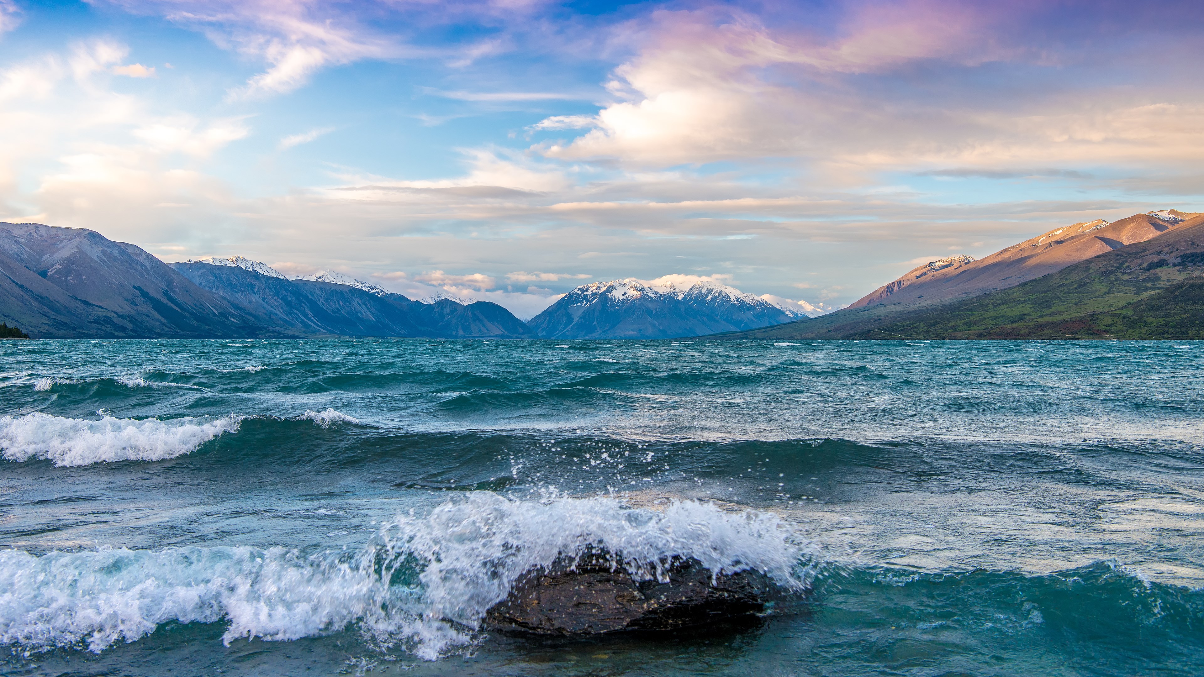 Waves crashing on a rock in a lake with mountains HD Wallpaper