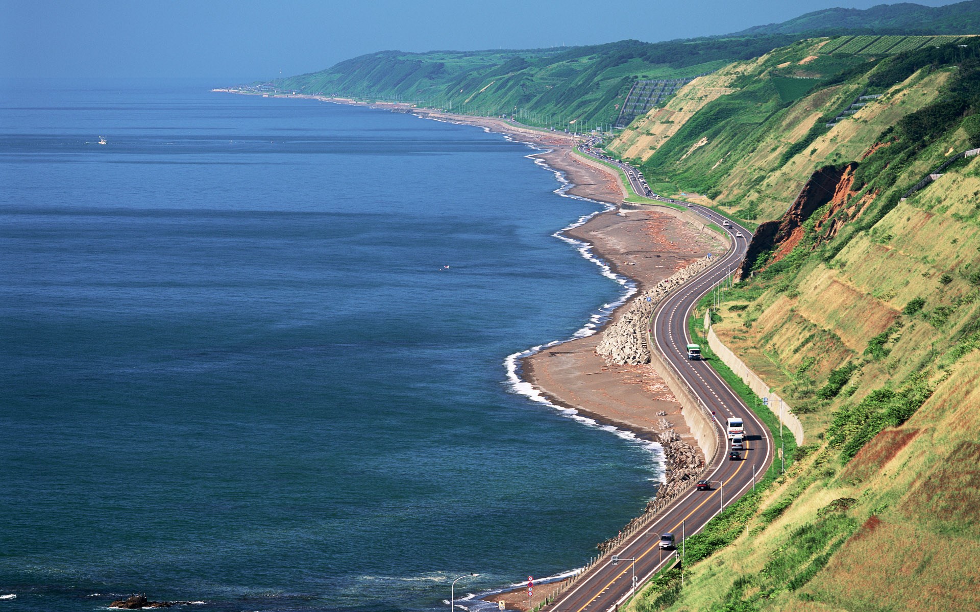 Coastal highway winding along the sea with green hills HD Wallpaper