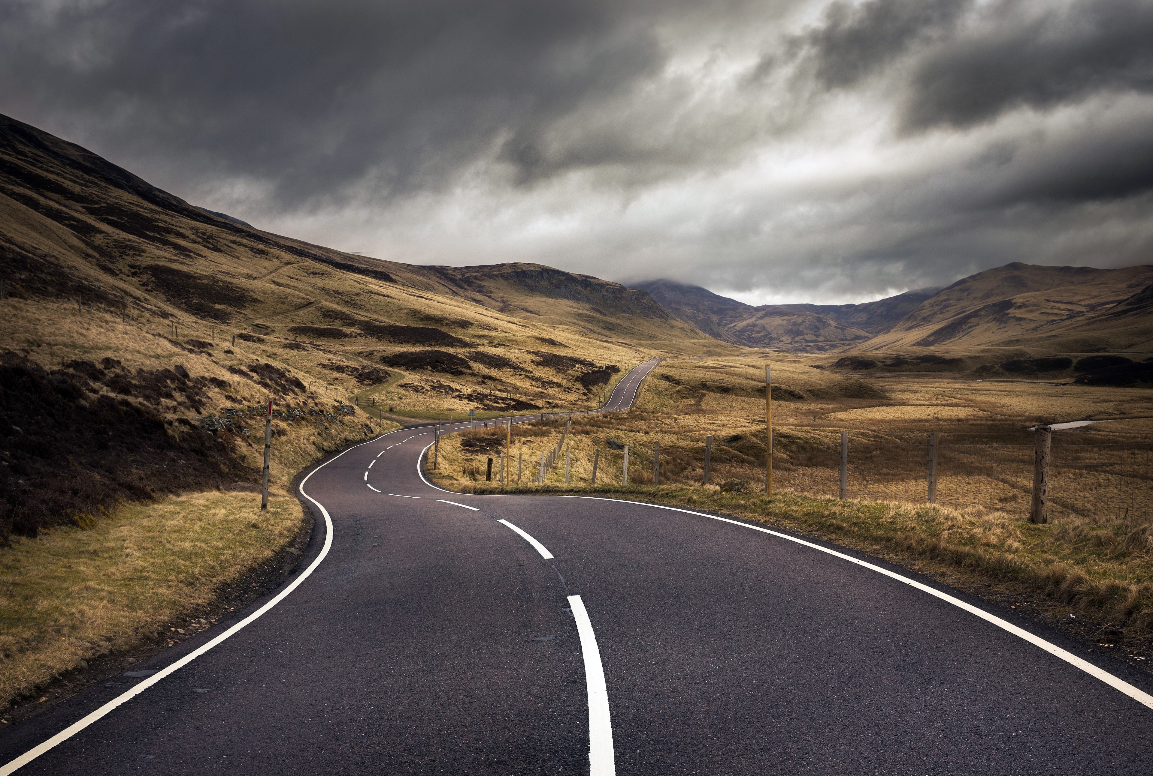 Winding road through a desolate landscape under stormy skies HD Wallpaper