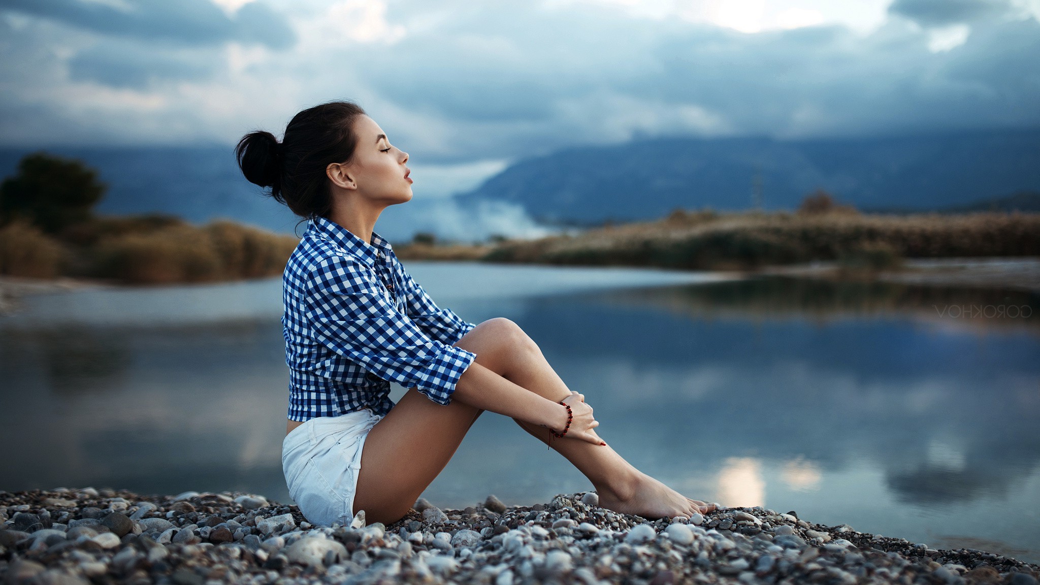 Woman with hair bun sitting by a lake HD Wallpaper