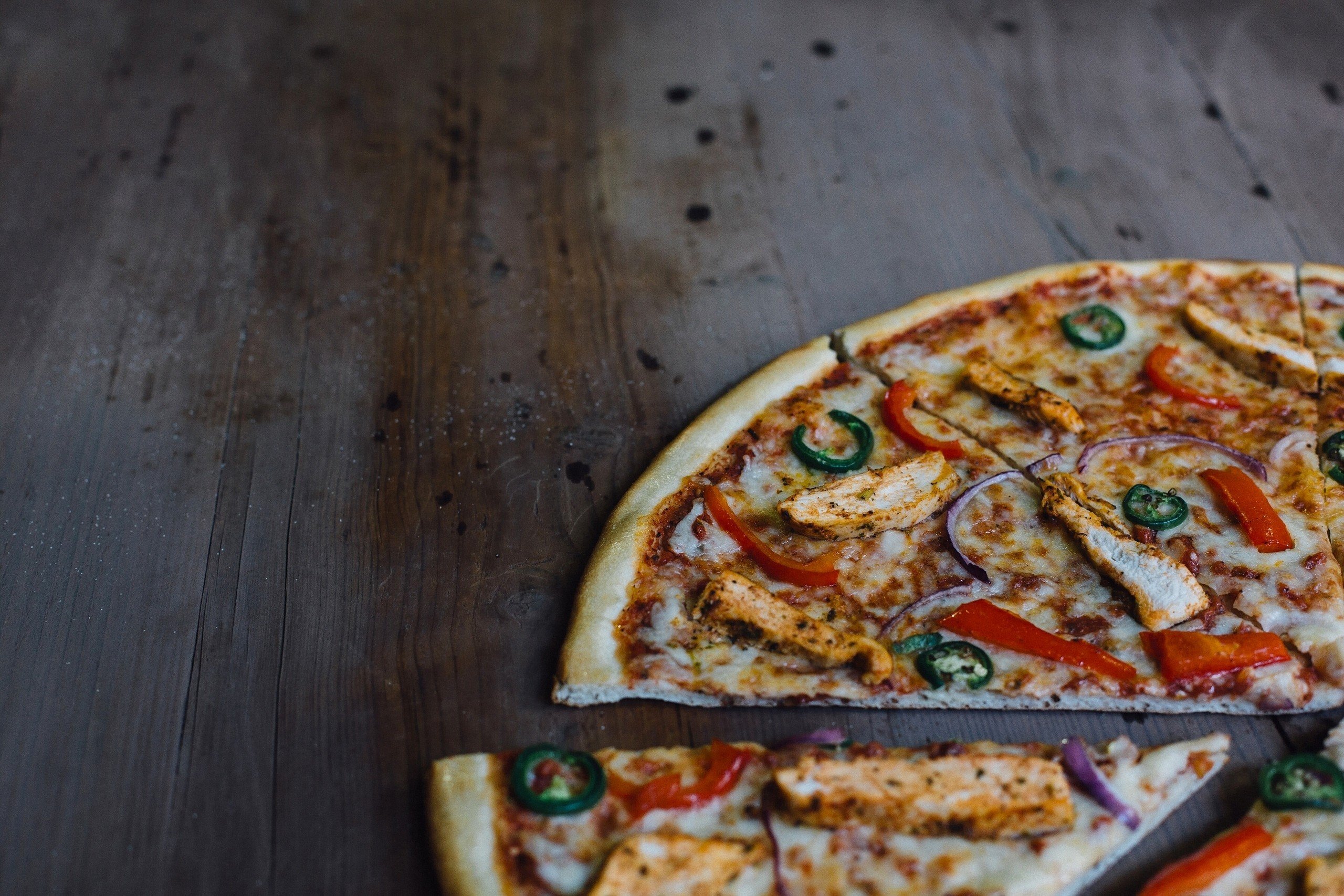 Pizza with chicken, peppers, and onions on a wooden table HD Wallpaper