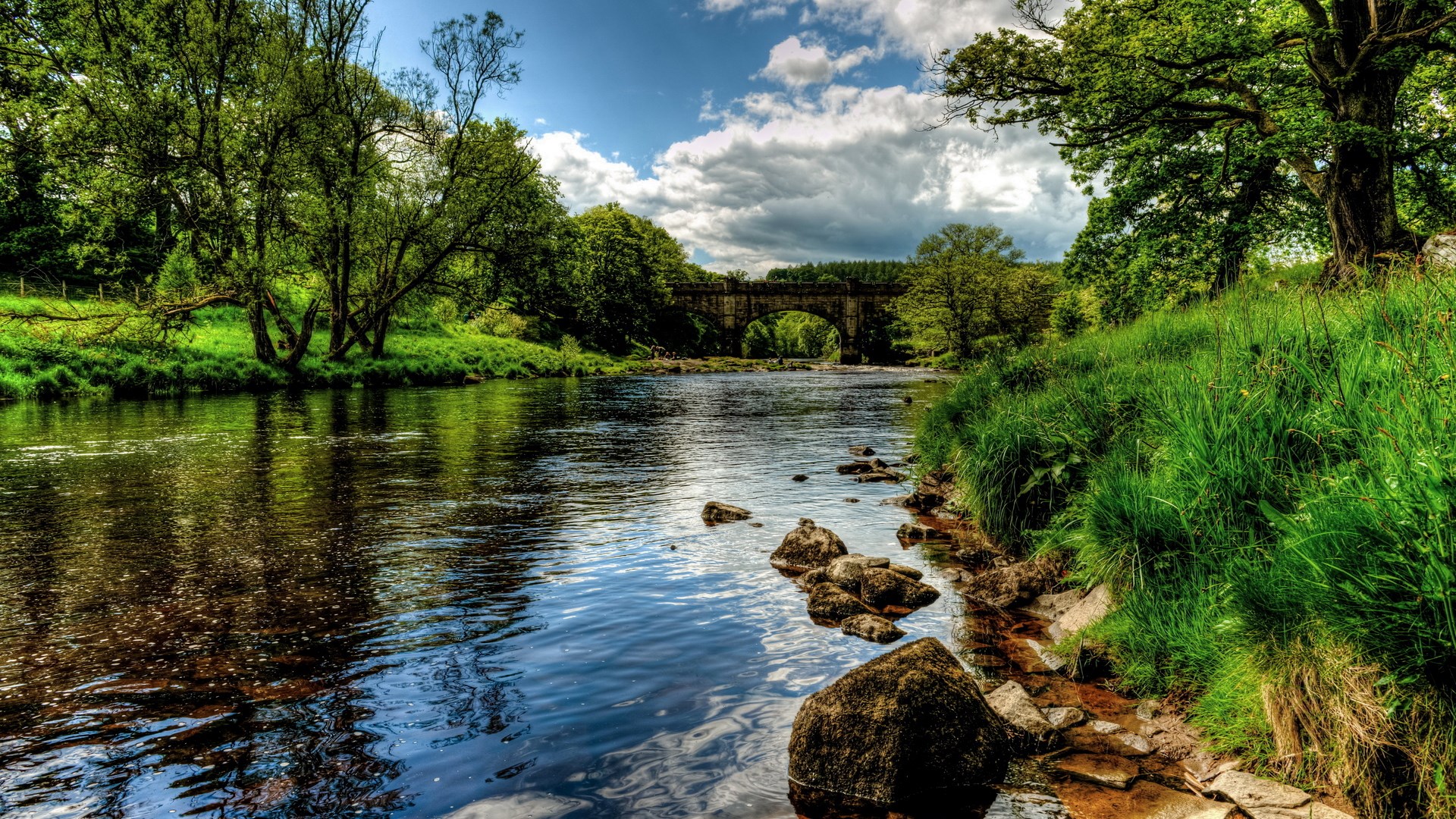 River flowing under a stone bridge surrounded by trees HD Wallpaper