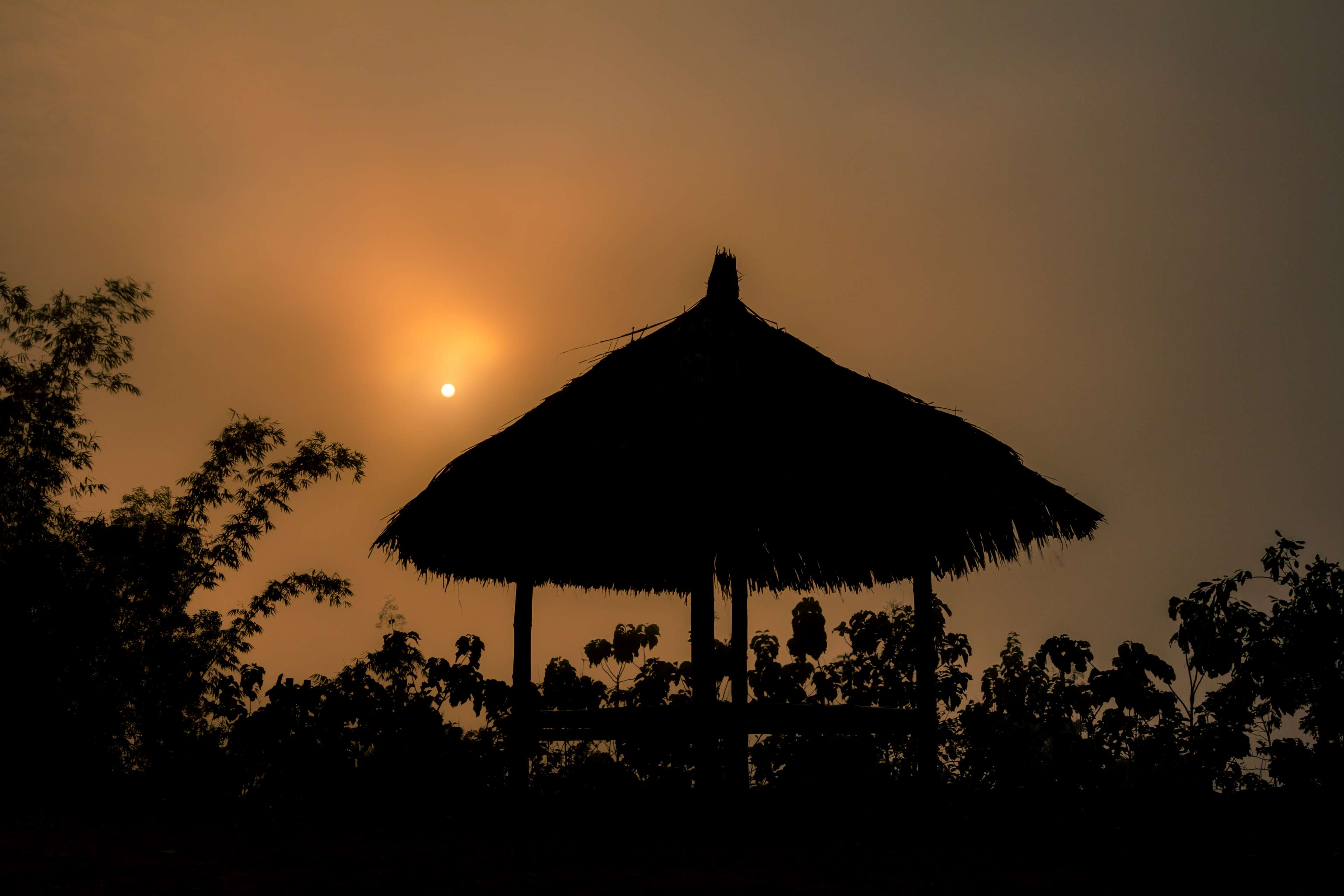 Silhouette of a thatched hut against a sunset HD Wallpaper
