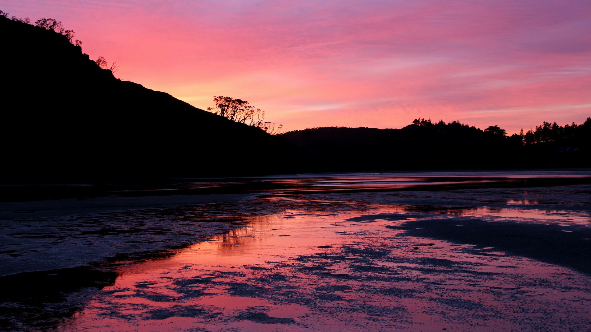 Sunset over a calm body of water with silhouetted hills HD Wallpaper