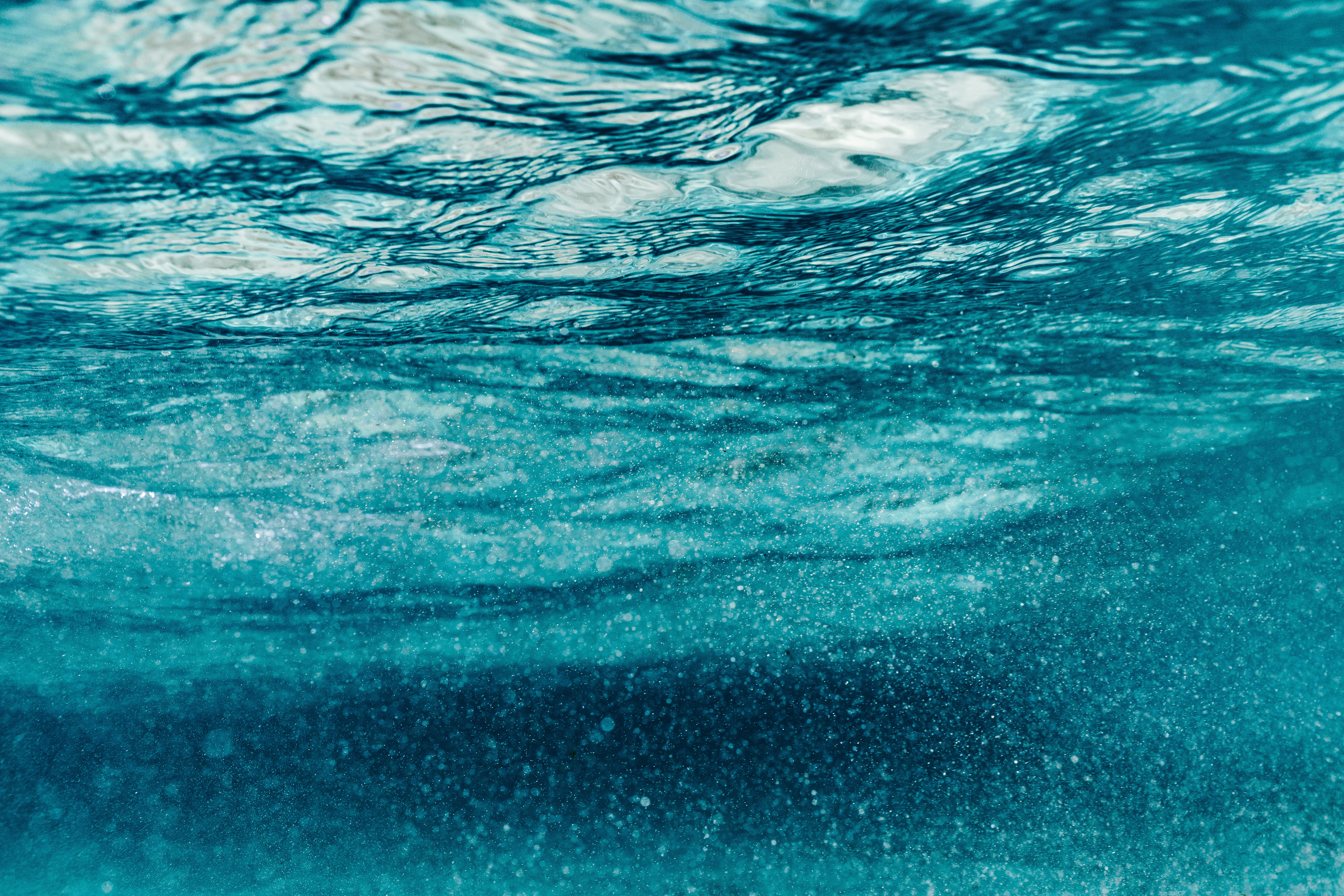 Underwater view of turquoise ocean water with ripples and bubbles HD Wallpaper