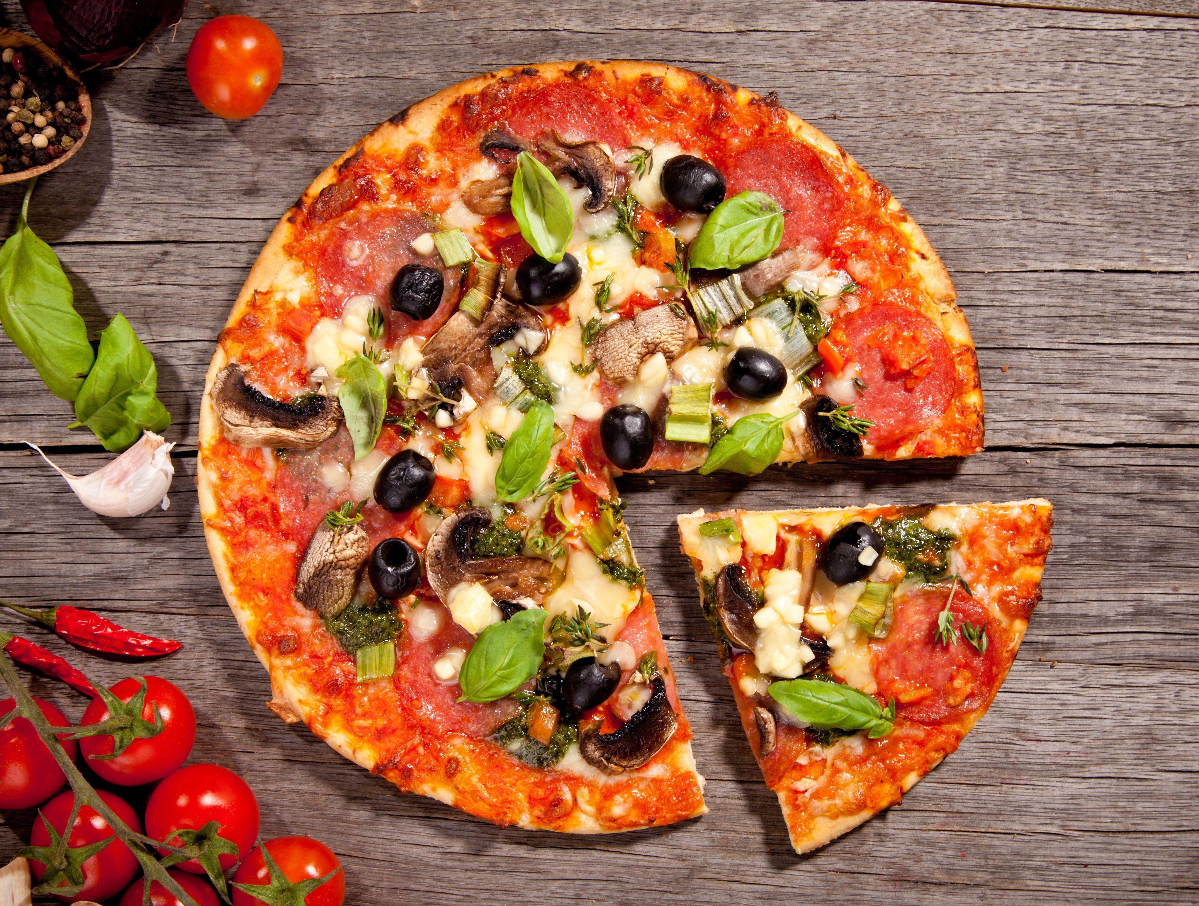 Pizza with salami, mushrooms, olives, and cheese on a wooden table HD Wallpaper