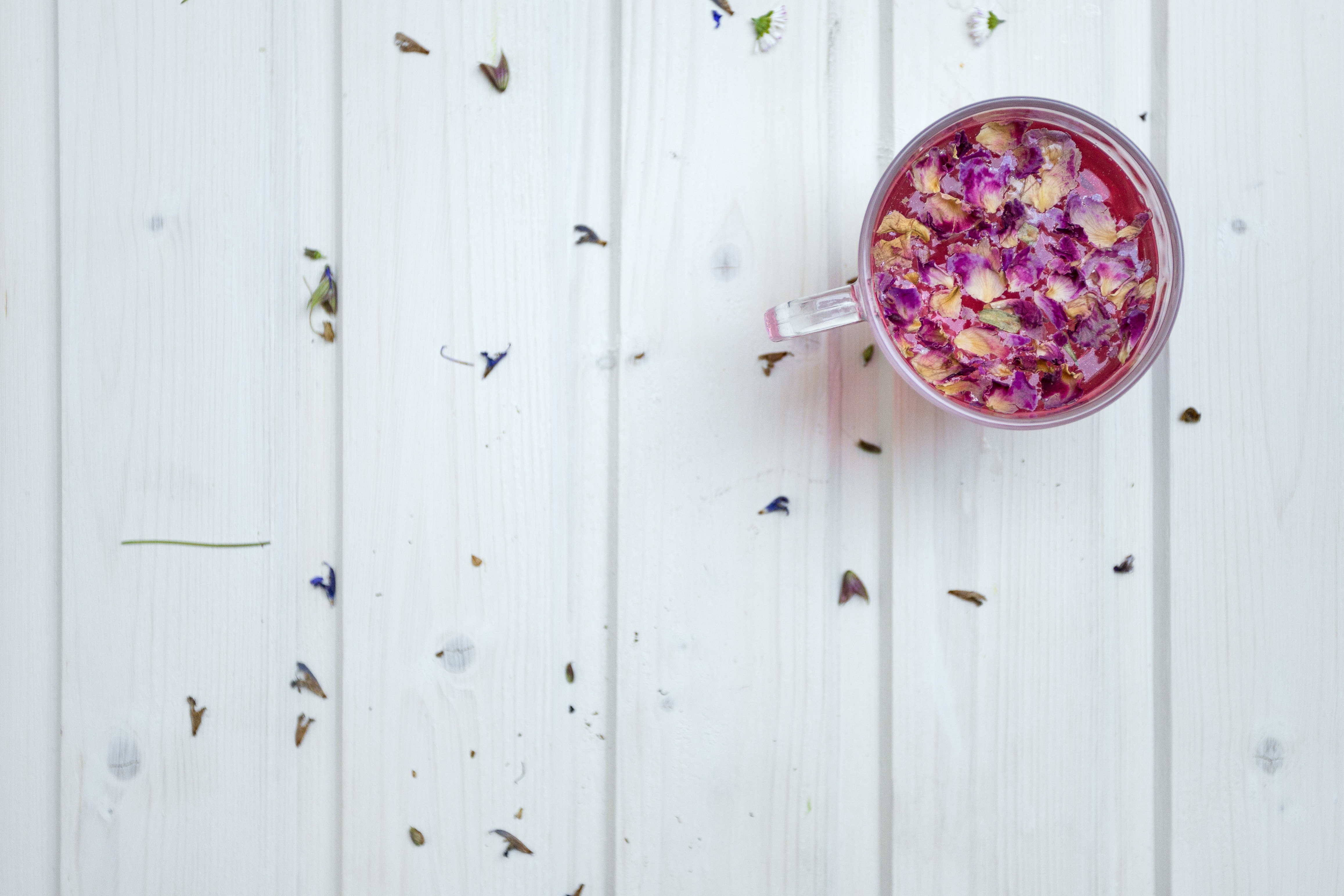 Floral tea with rose petals in a glass cup on a white wooden table HD Wallpaper