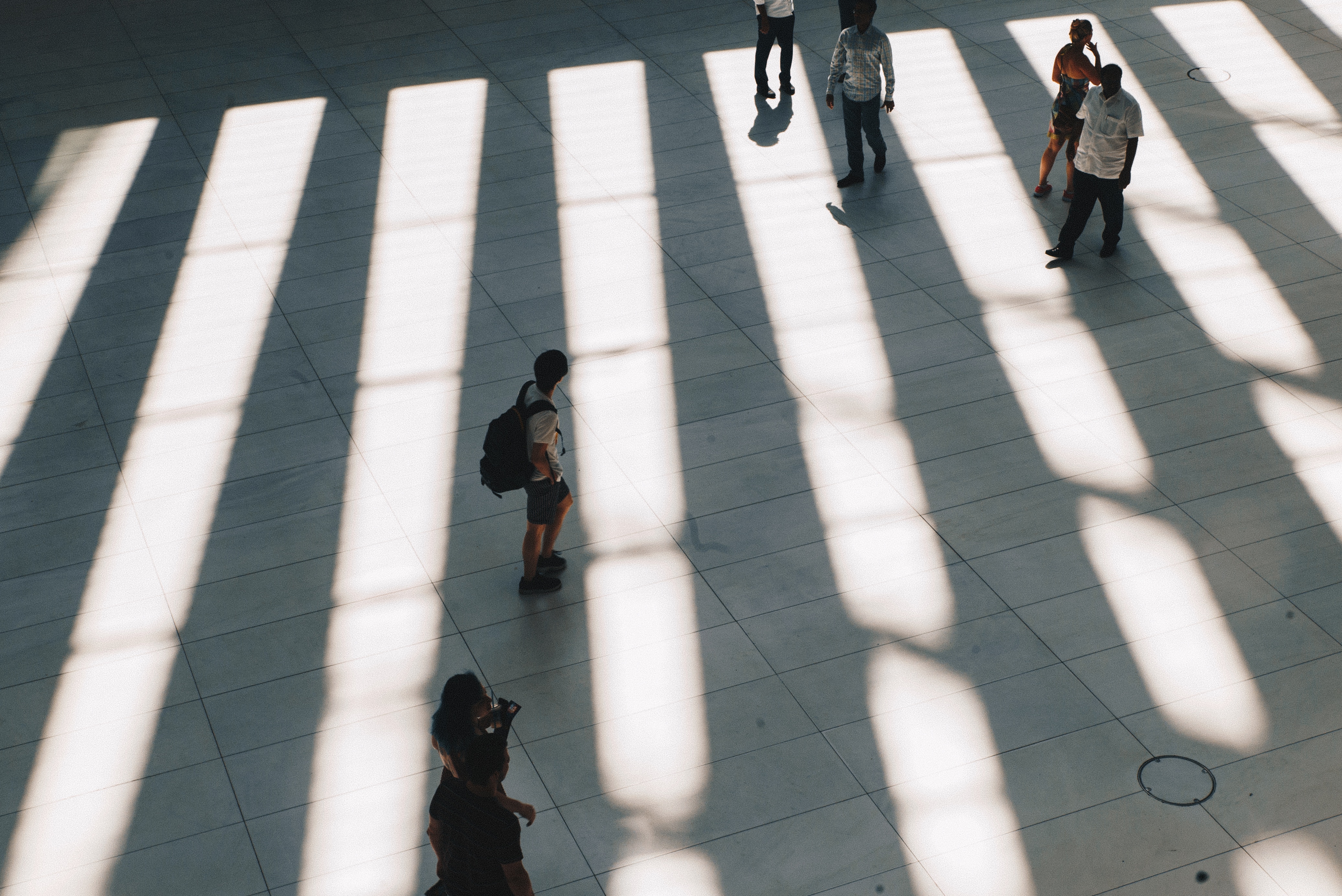 People walking in a sunlit hall with striped shadows HD Wallpaper