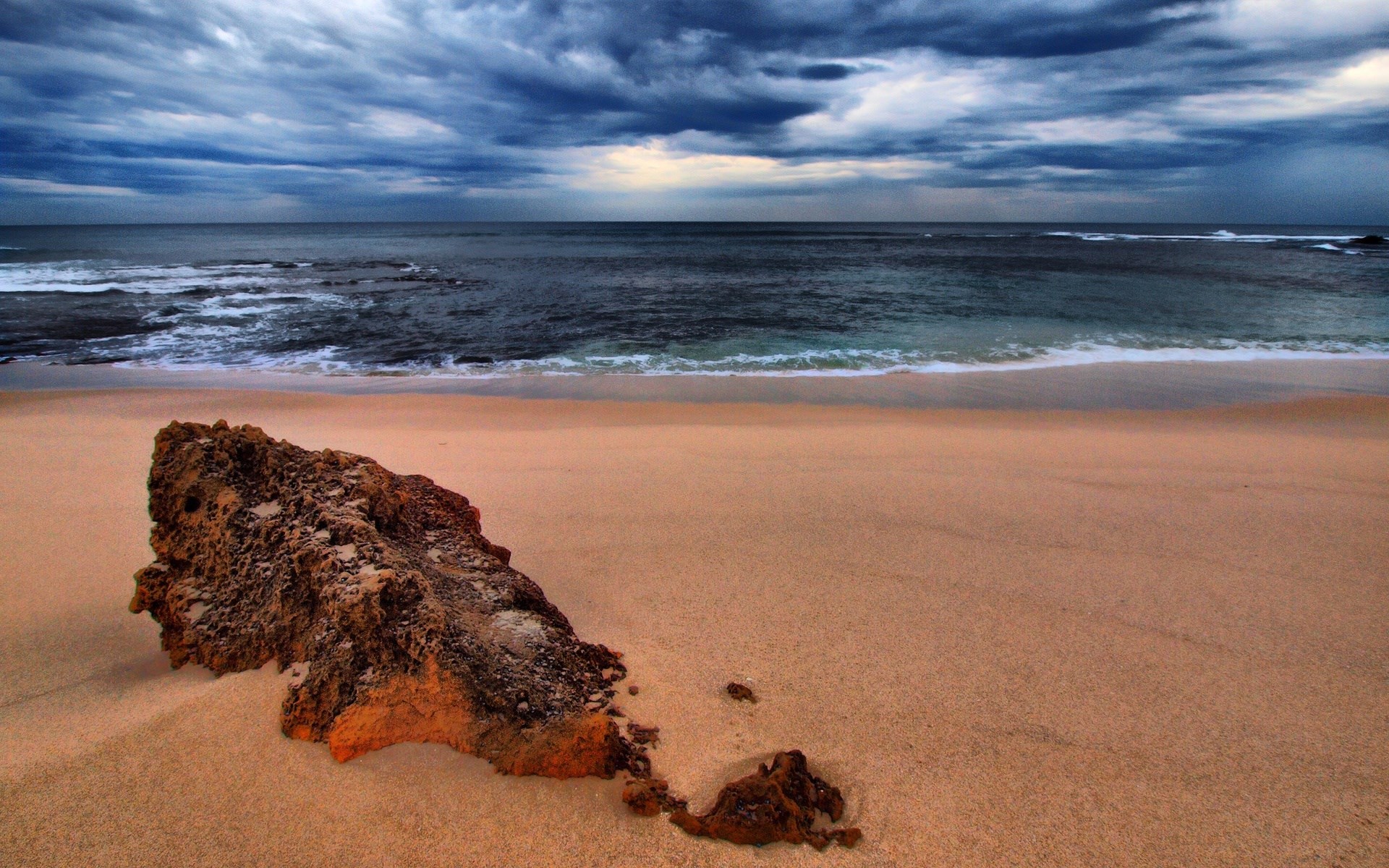 A large rock on a sandy beach with stormy ocean waves. HD Wallpaper