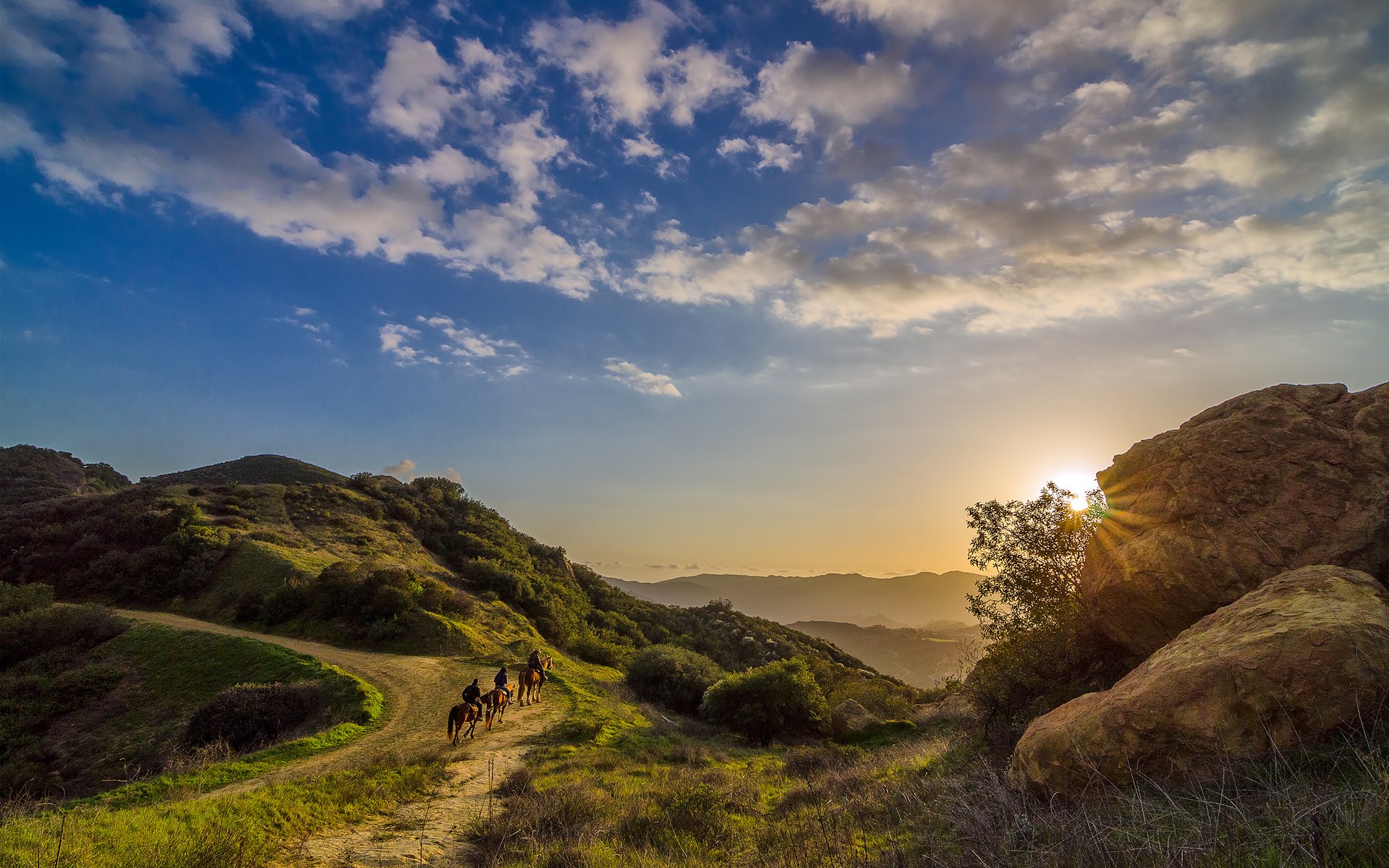 People riding horses on a mountain trail at sunset HD Wallpaper