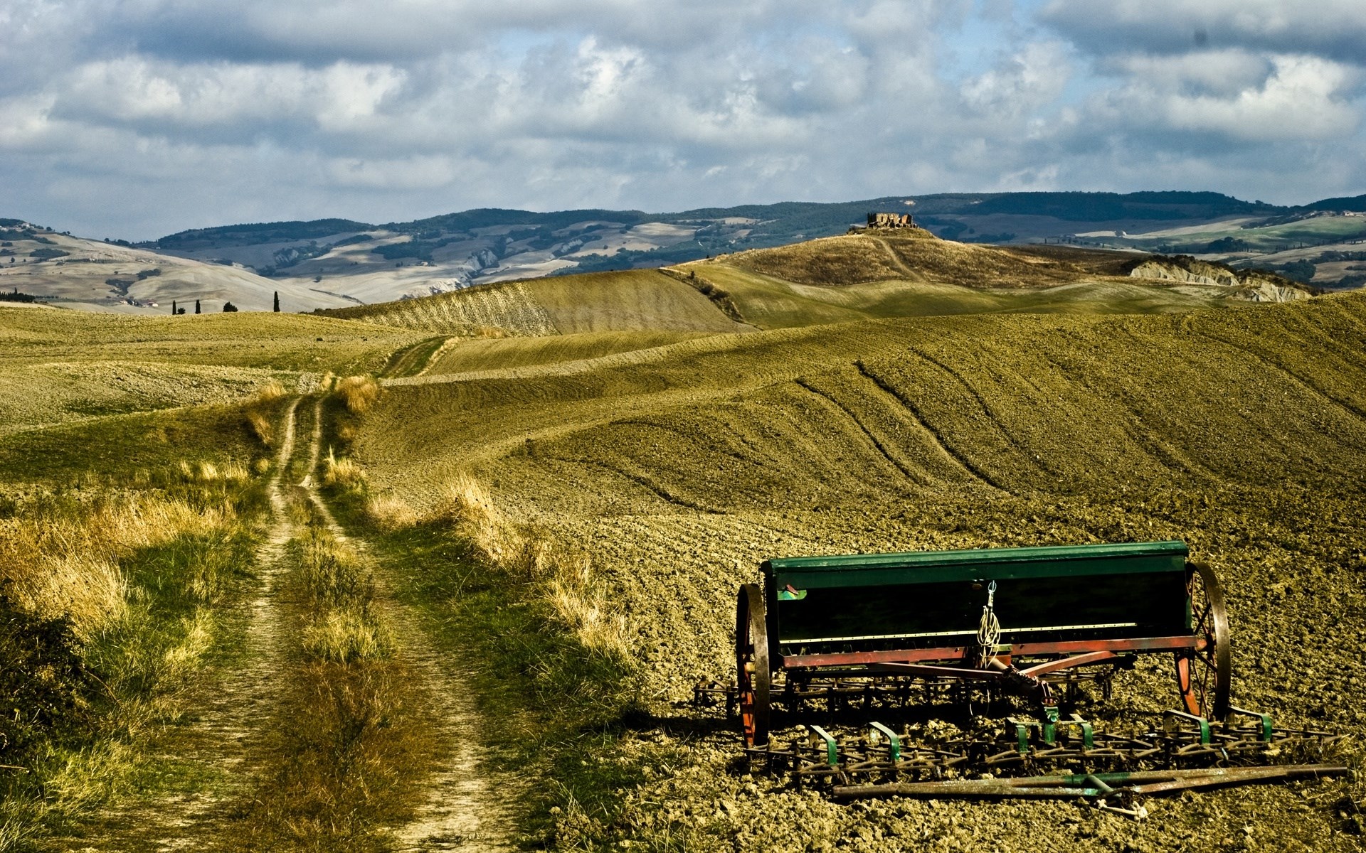 Tuscan landscape with a farm implement and rolling hills HD Wallpaper