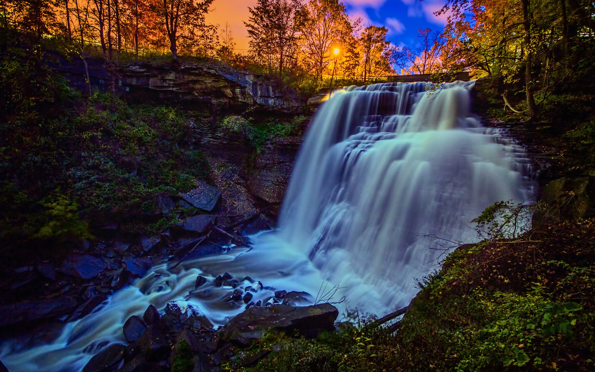 Waterfall cascading through a forest during autumn HD Wallpaper
