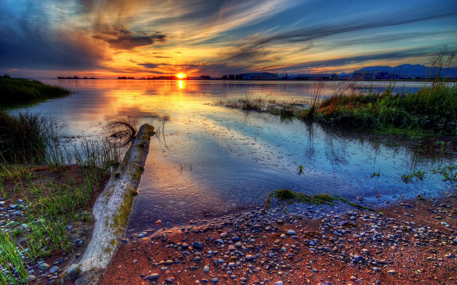 Sunset over a calm body of water with a log on the shore HD Wallpaper