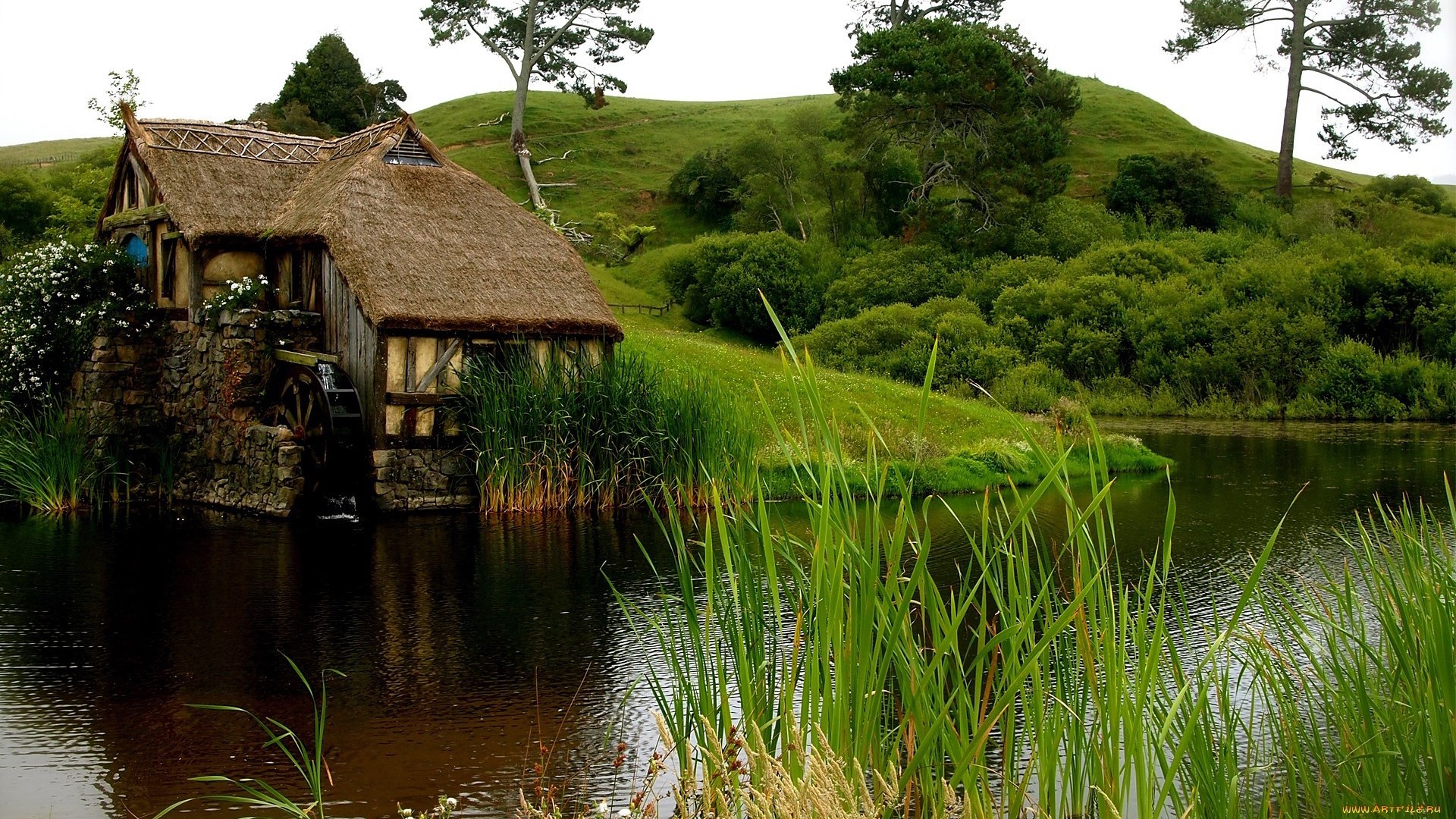 Hobbiton watermill by a lake with rolling hills HD Wallpaper
