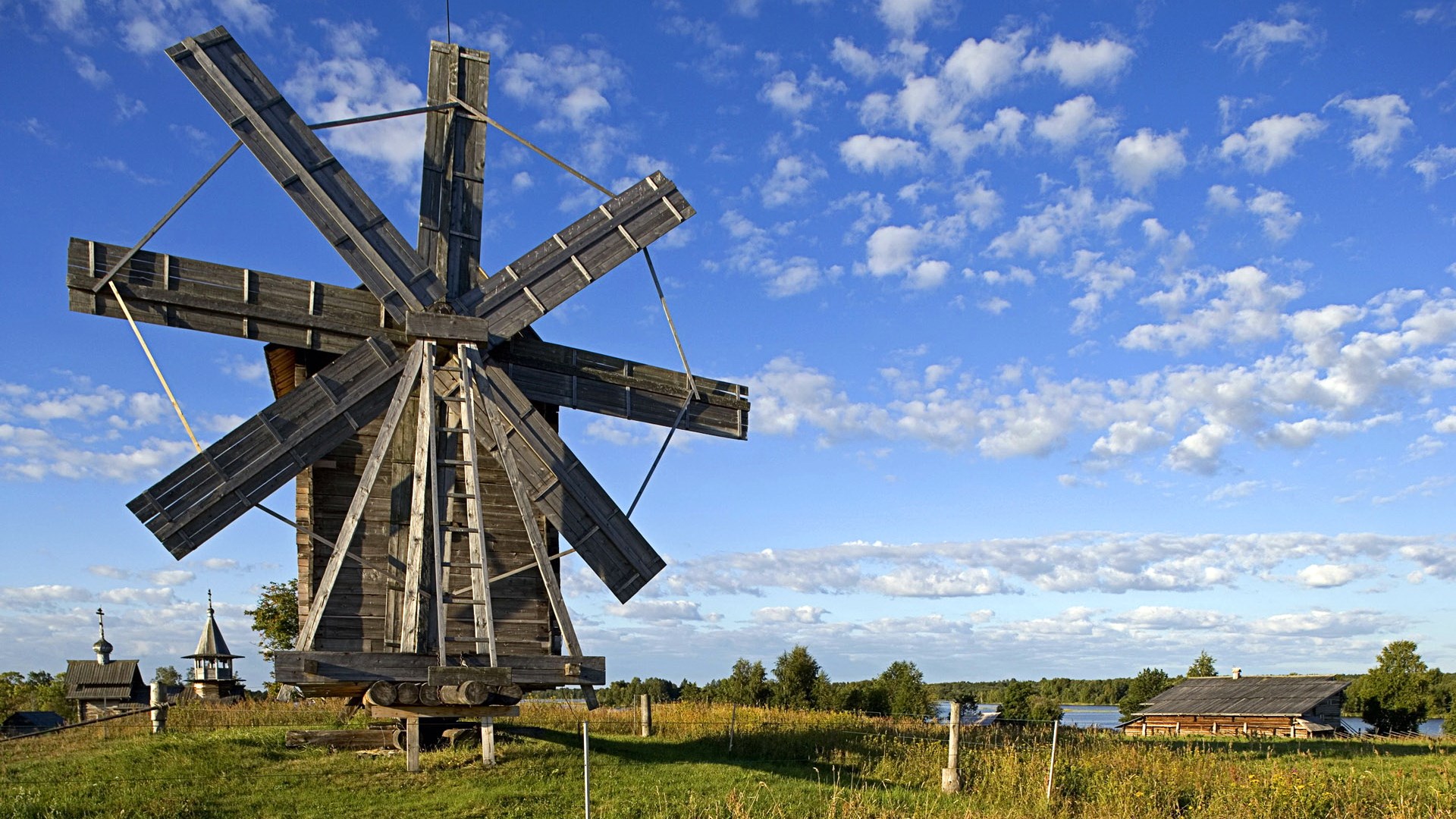 Wooden windmill and traditional buildings under a blue sky HD Wallpaper