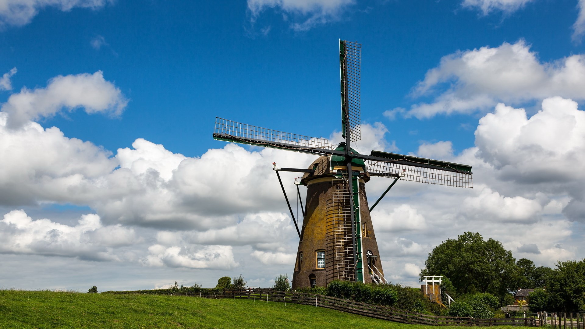 Windmill on a grassy hill under a cloudy blue sky HD Wallpaper