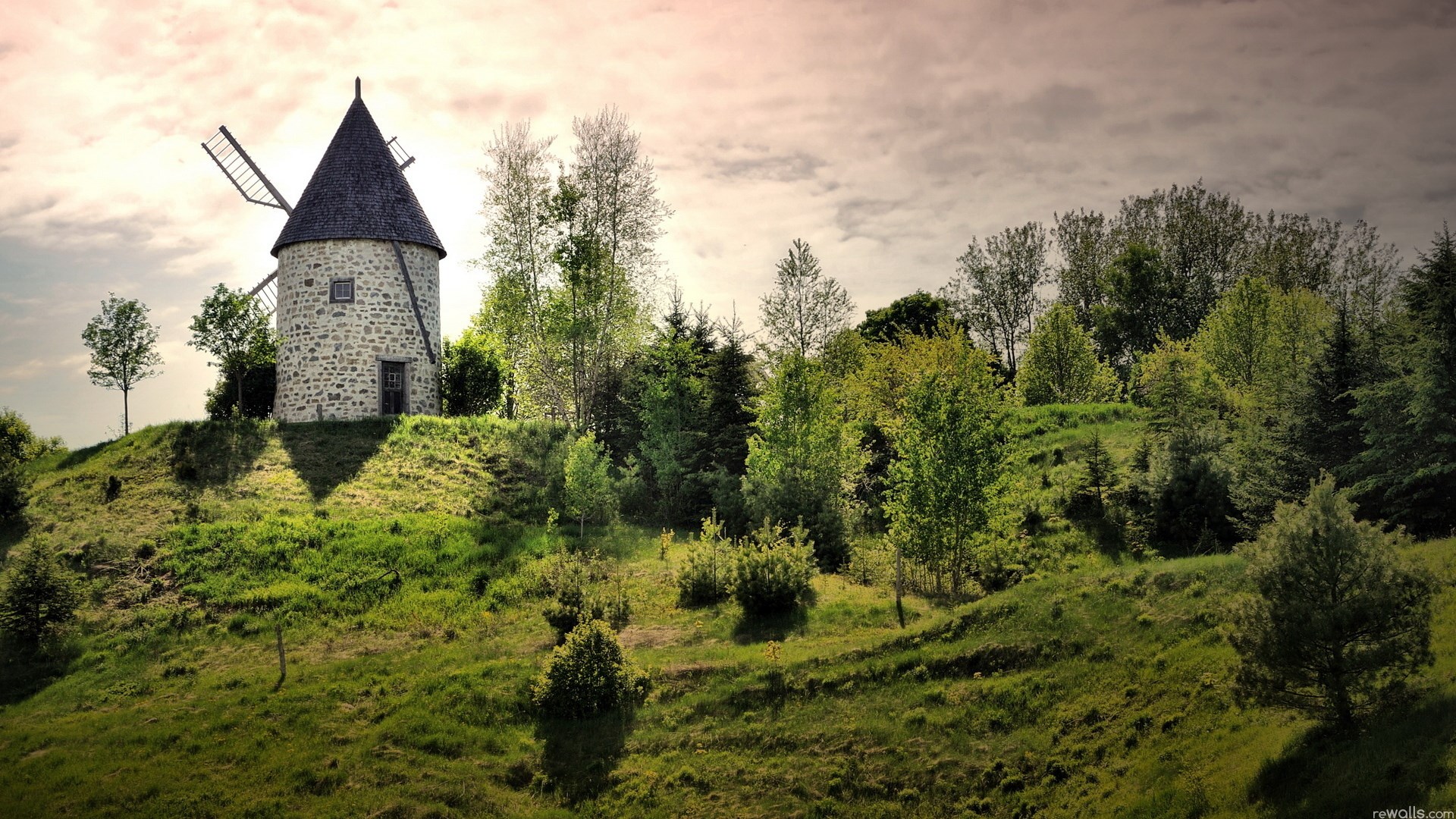 Stone windmill on a grassy hill with trees HD Wallpaper