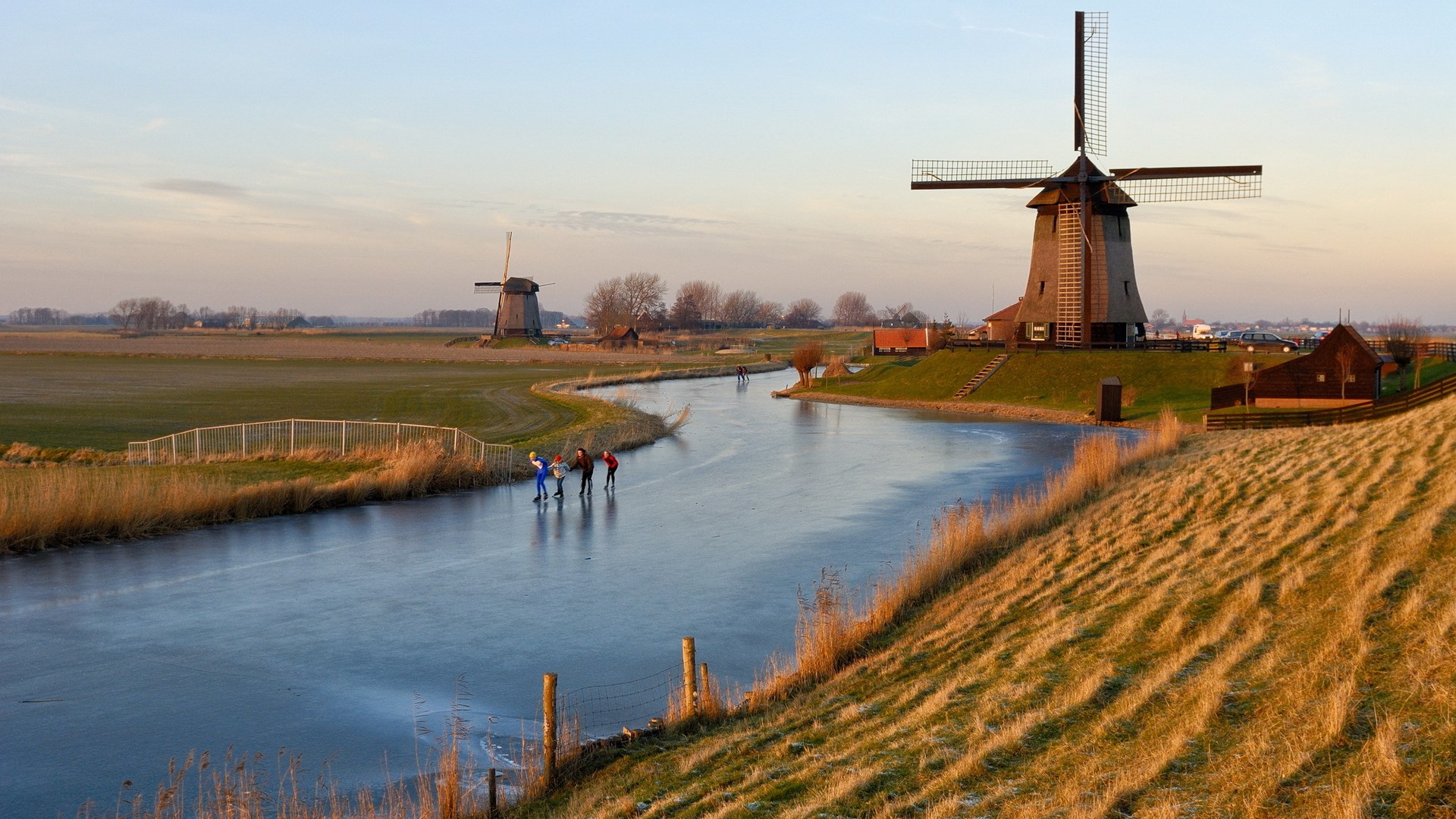 People ice skating near windmills at sunset HD Wallpaper