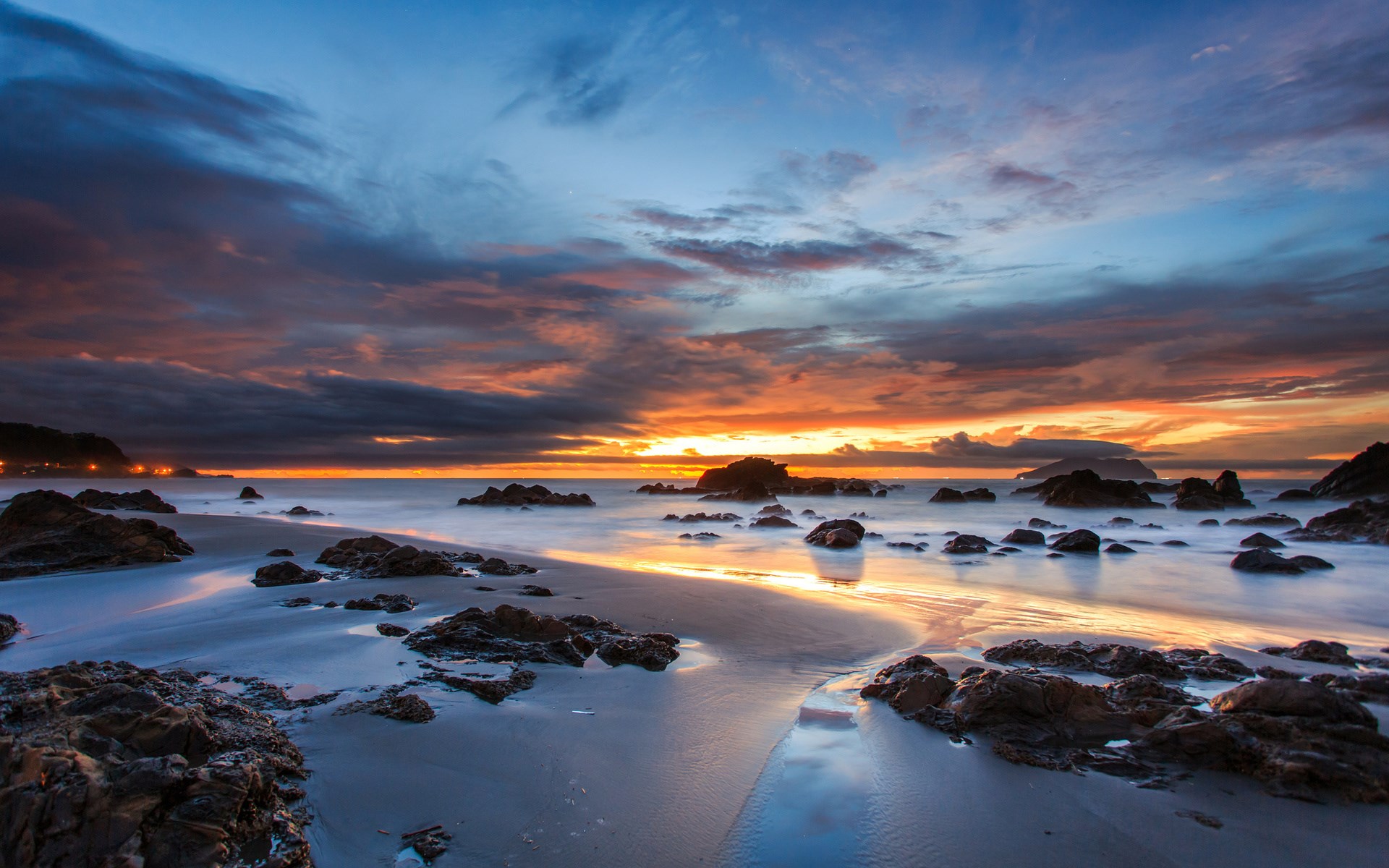 Sunset over a rocky beach with calm ocean waves HD Wallpaper