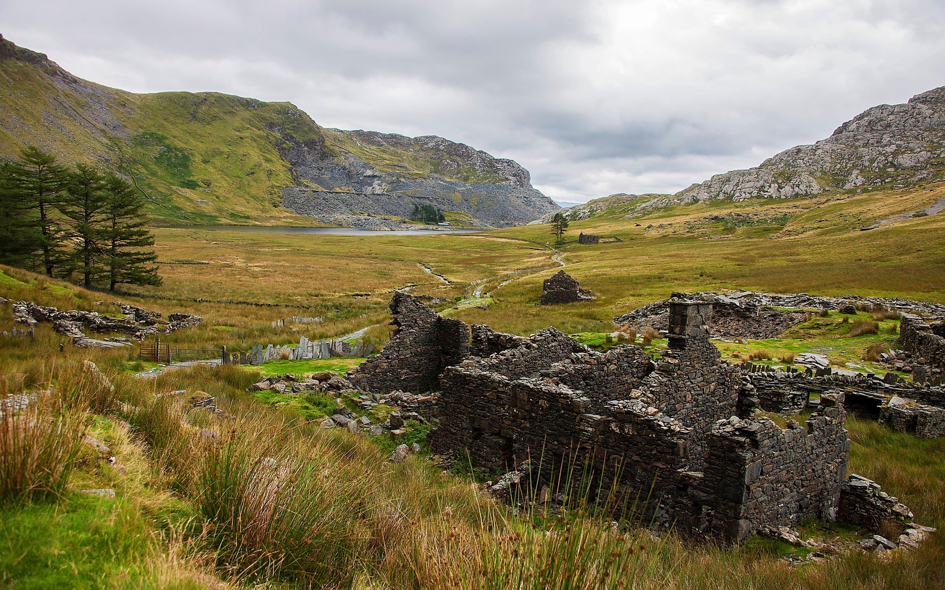 Ruined stone buildings in a grassy valley with mountains HD Wallpaper