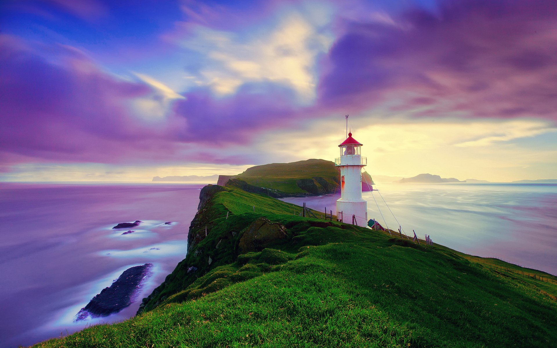 Lighthouse on a grassy cliff overlooking the ocean at sunset HD Wallpaper