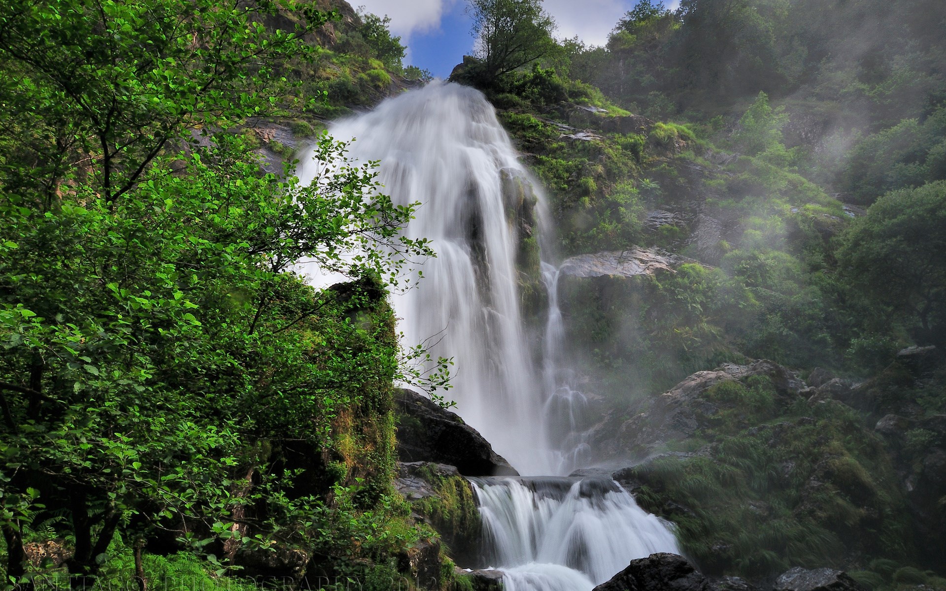 Waterfall cascading down a rocky, moss-covered cliff face HD Wallpaper