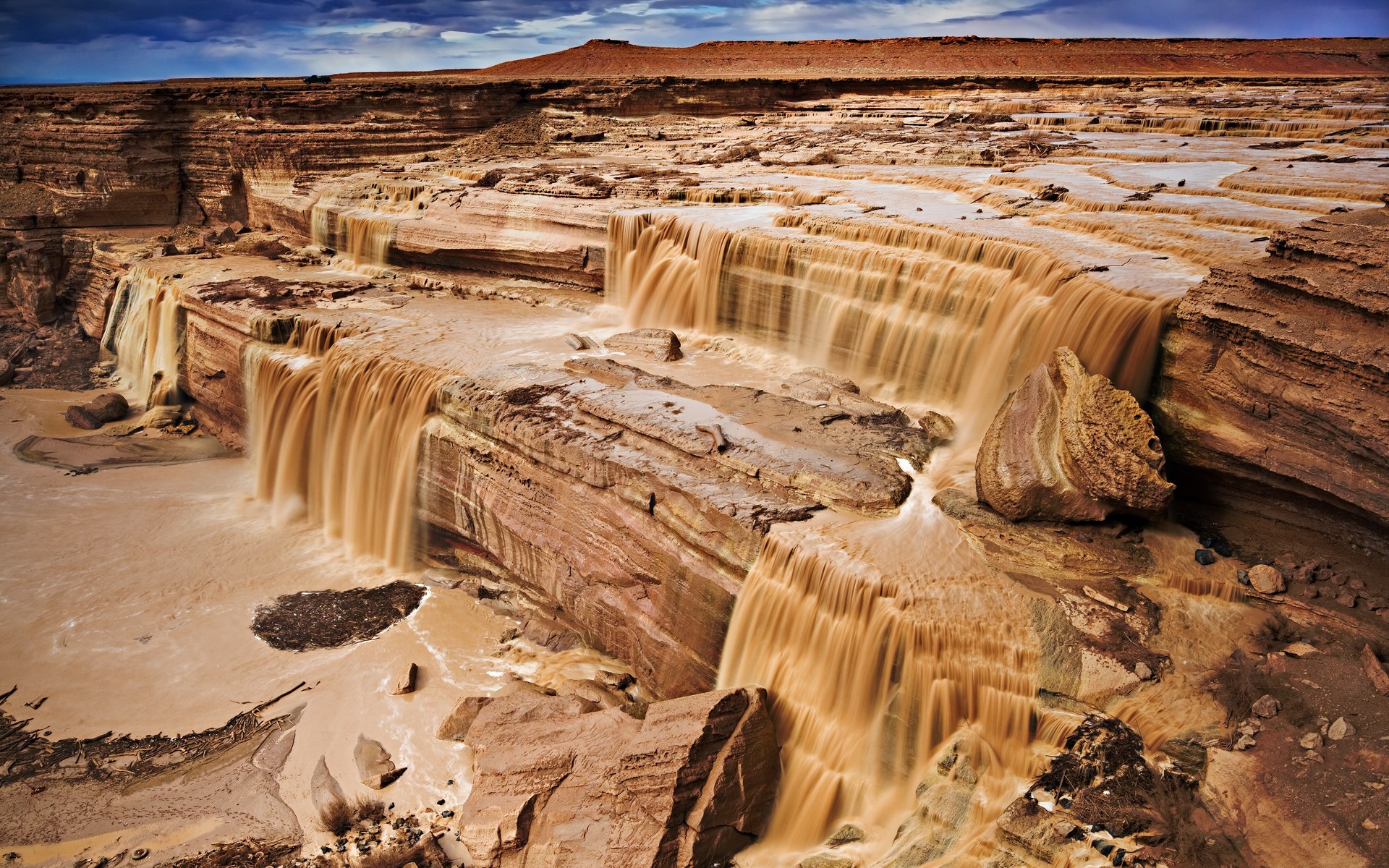 Muddy waterfalls cascading over layered rock formations HD Wallpaper