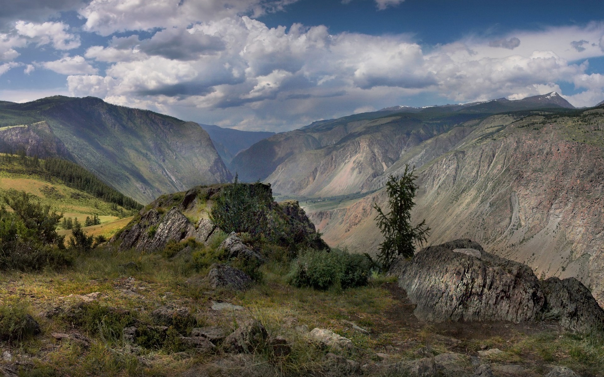 Mountain valley with rocky foreground and cloudy sky HD Wallpaper