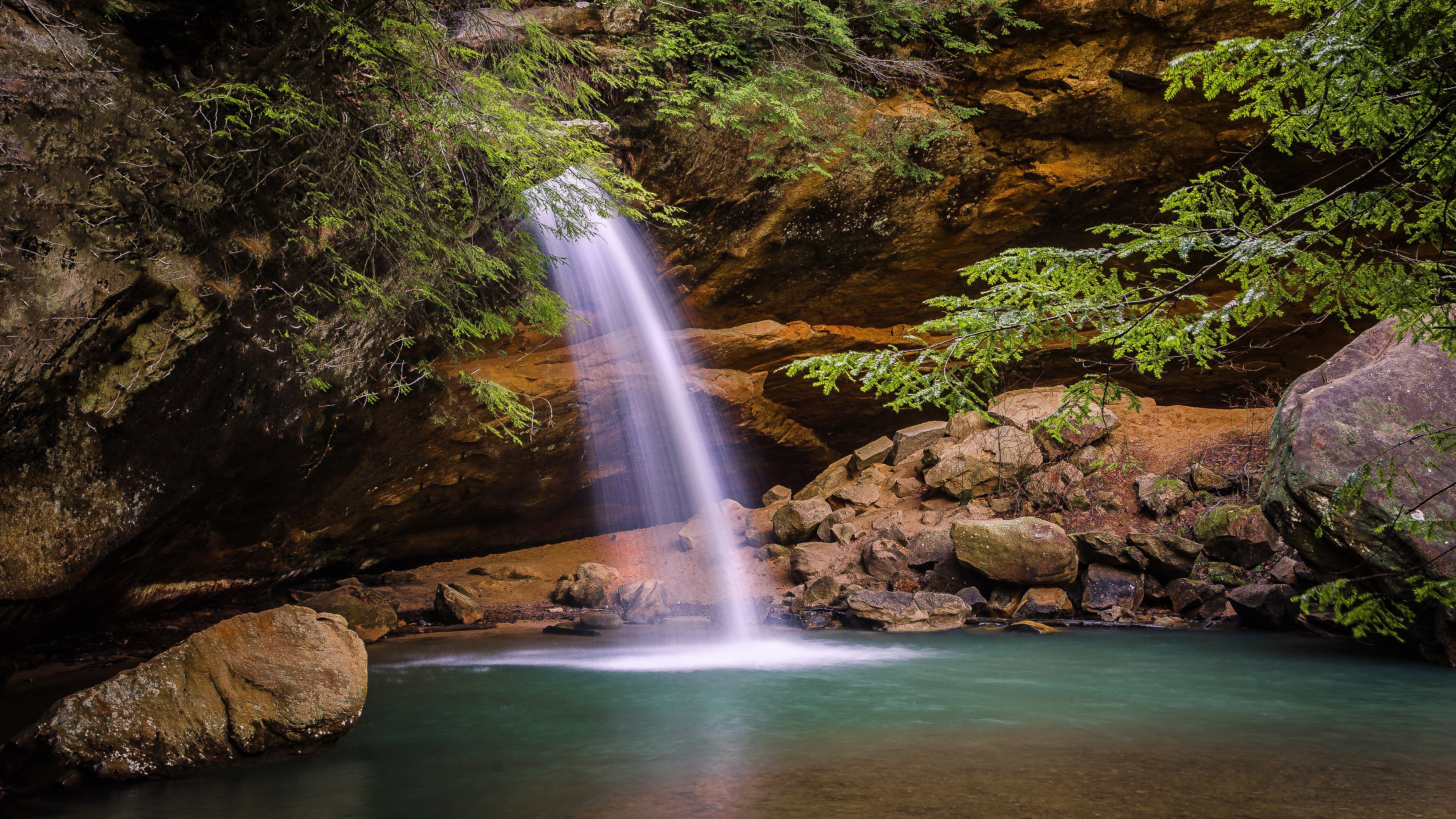 Waterfall cascading into a turquoise pool in a rocky grotto HD Wallpaper