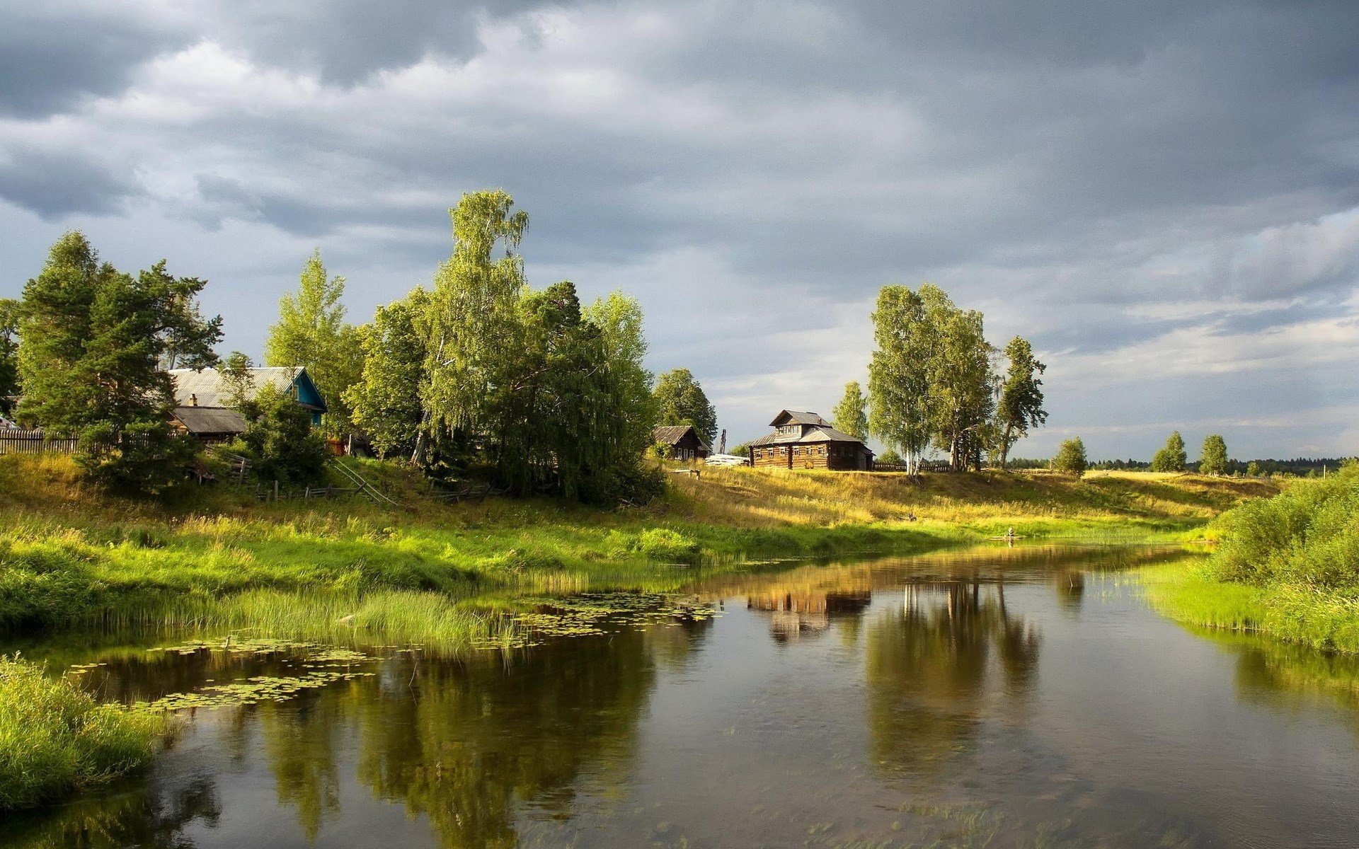 Rural village by a river under a cloudy sky HD Wallpaper