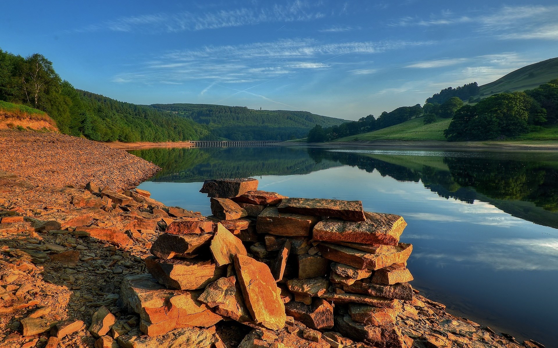 Rocky shore of a reservoir with a dam in the distance HD Wallpaper