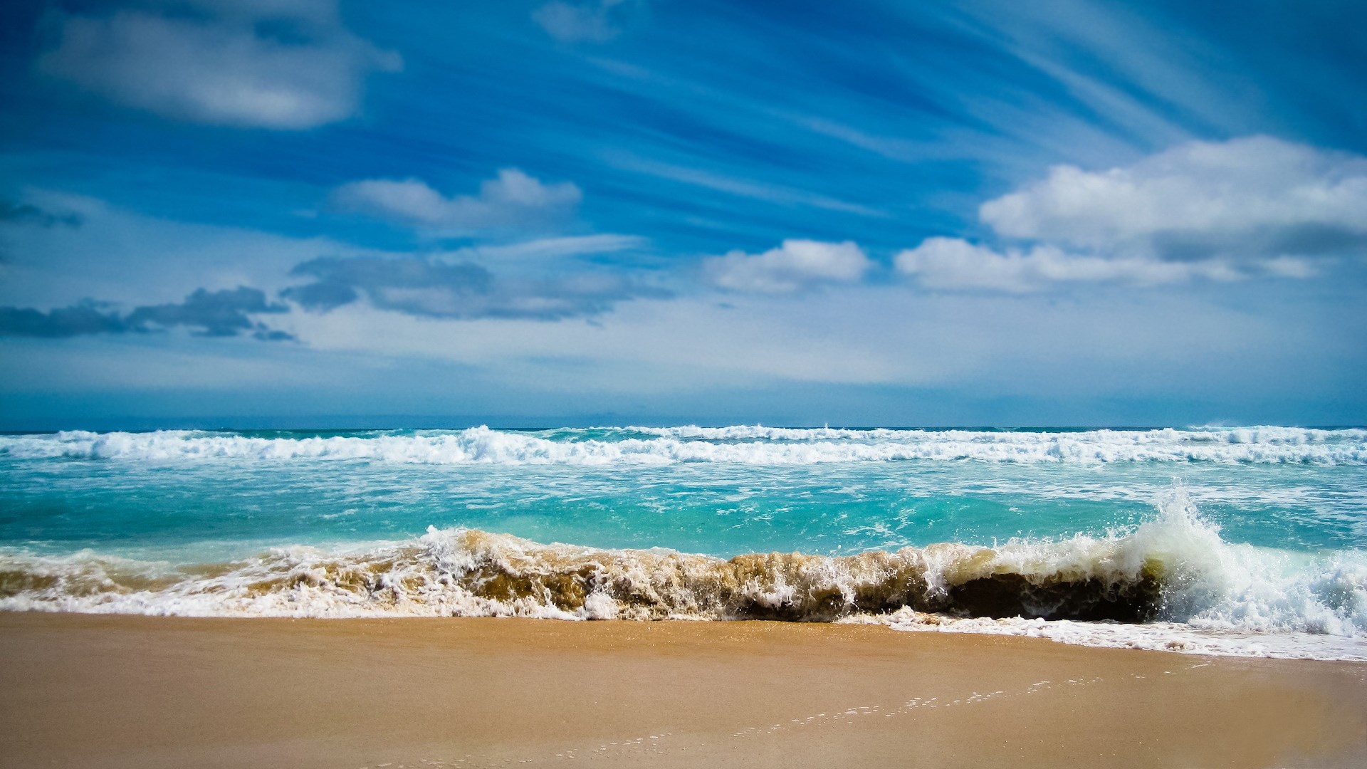 Ocean waves crashing on a sandy beach under a cloudy sky HD Wallpaper