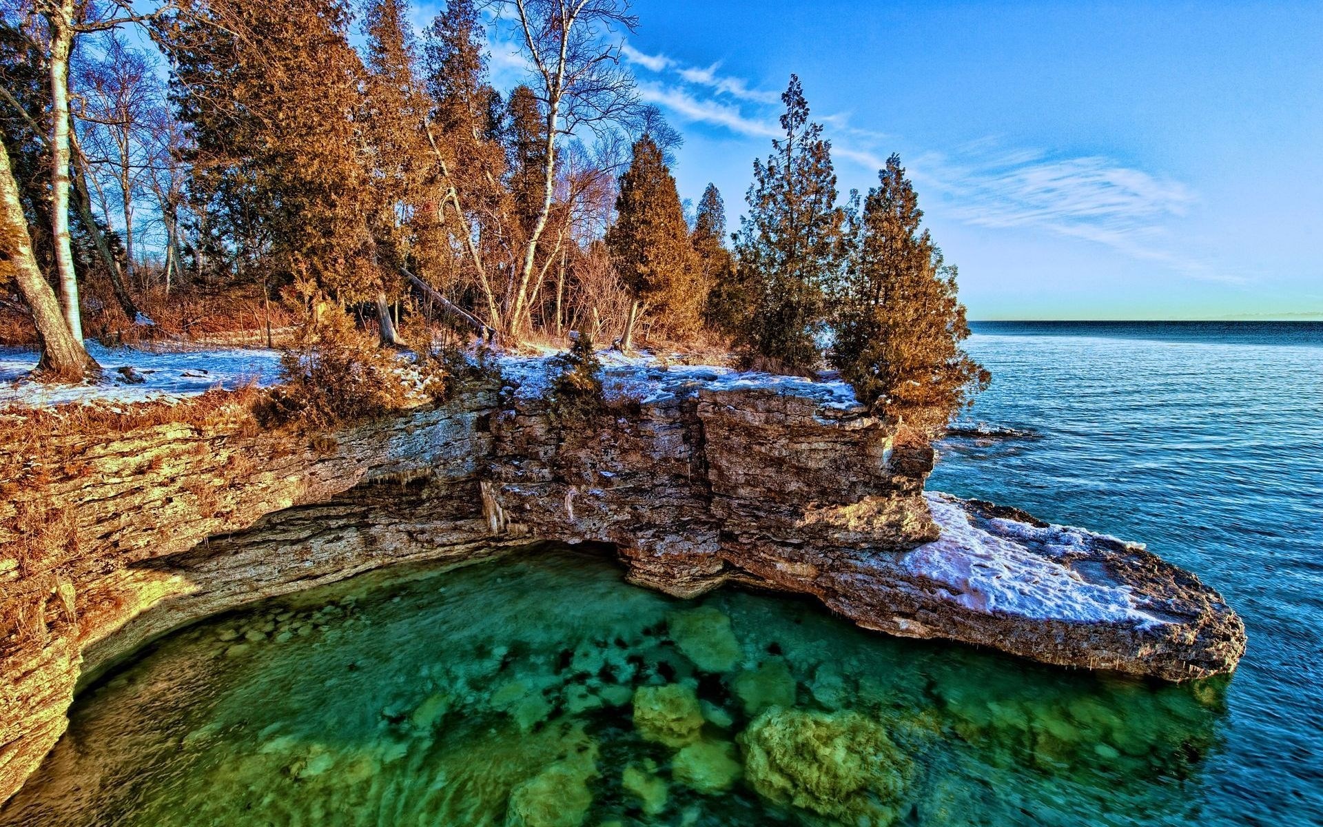 Rocky cliff overlooking clear turquoise water and forest HD Wallpaper