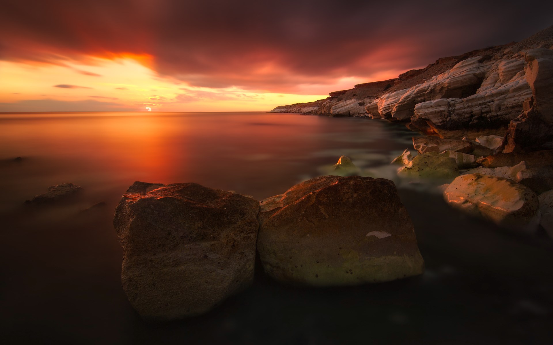 Sunset over rocky coastline with calm sea HD Wallpaper