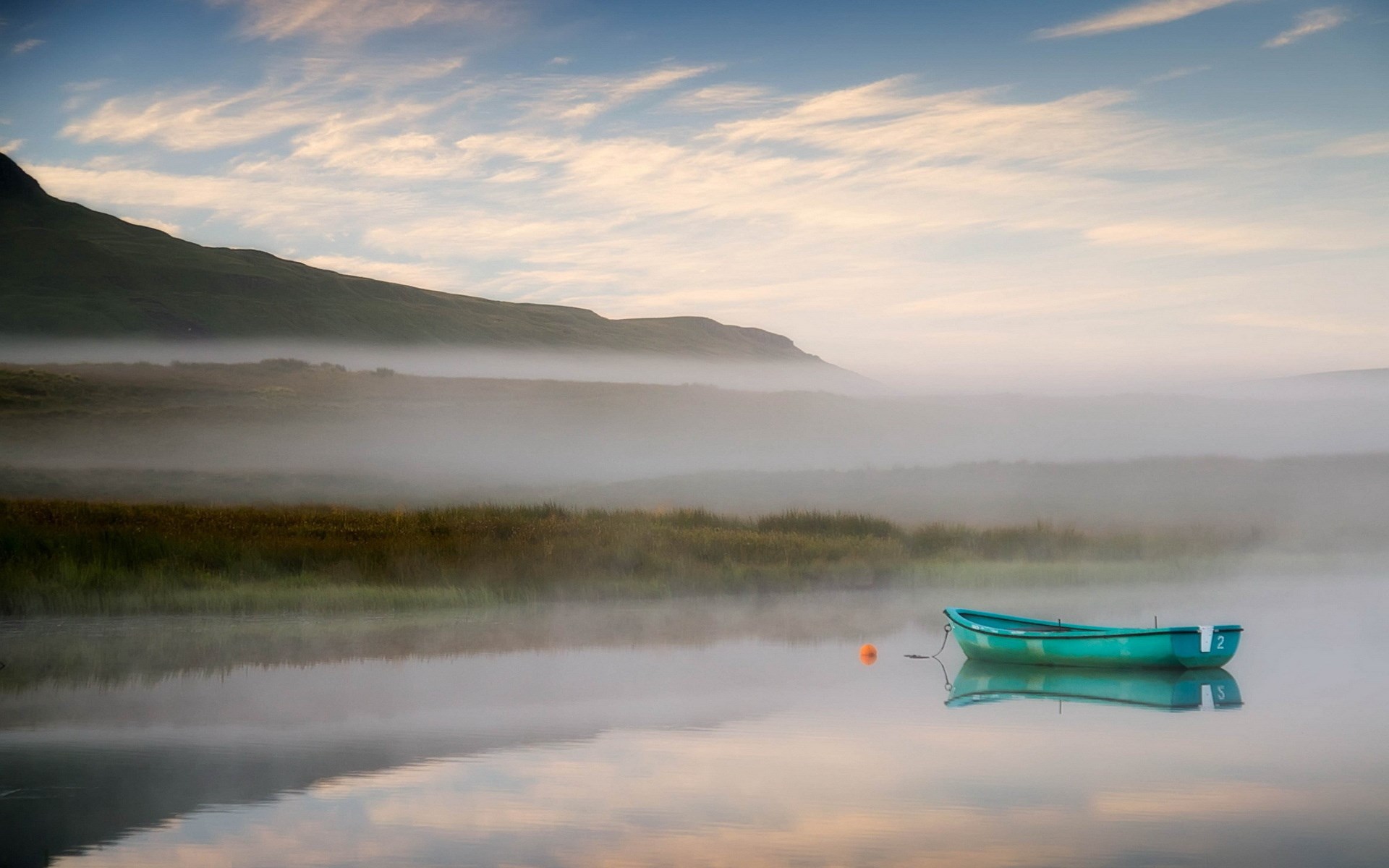 A teal rowboat floats on a misty lake HD Wallpaper
