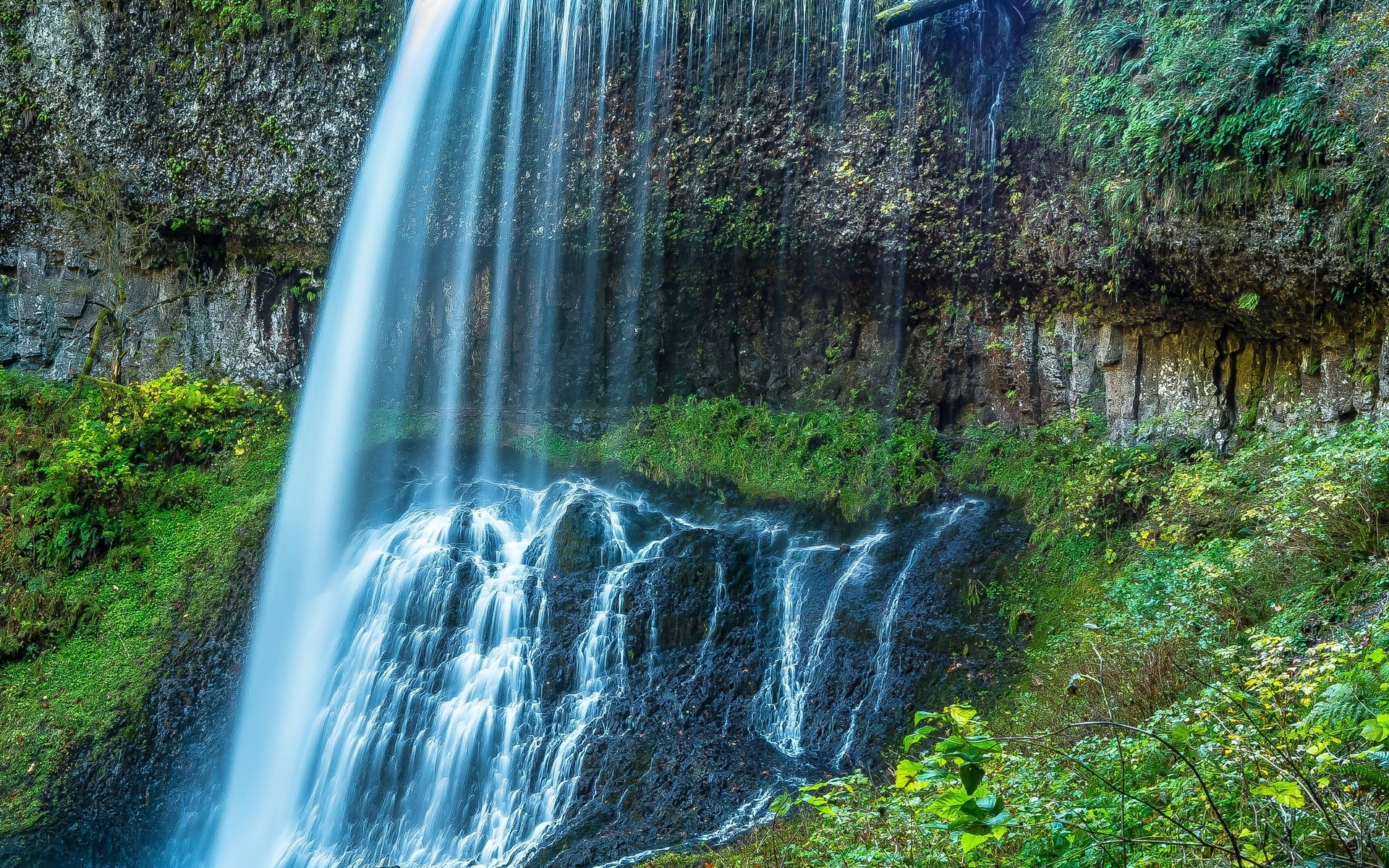 Waterfall cascading over mossy rocks and greenery HD Wallpaper
