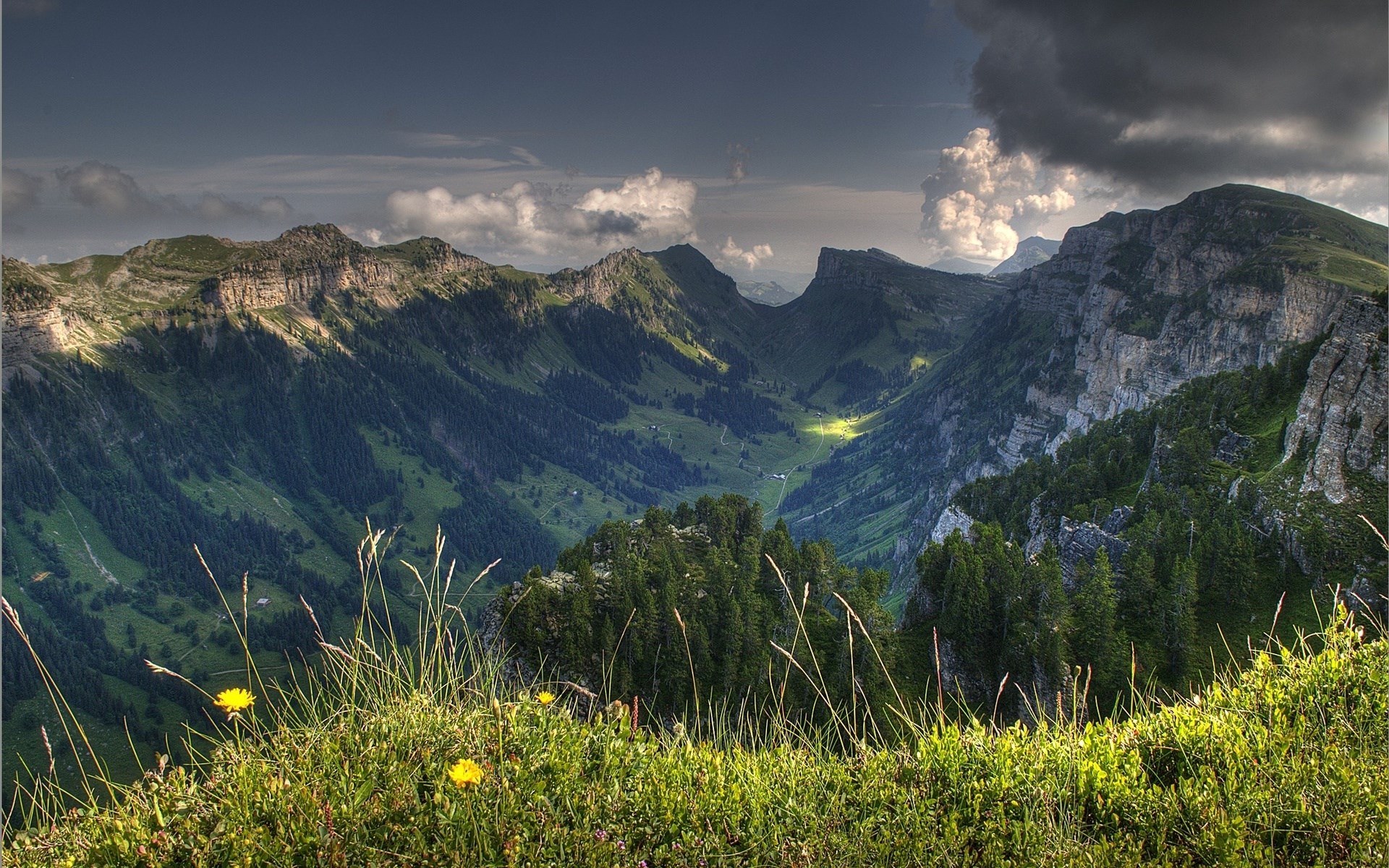 Sunlit valley between green mountains with grass in foreground HD Wallpaper