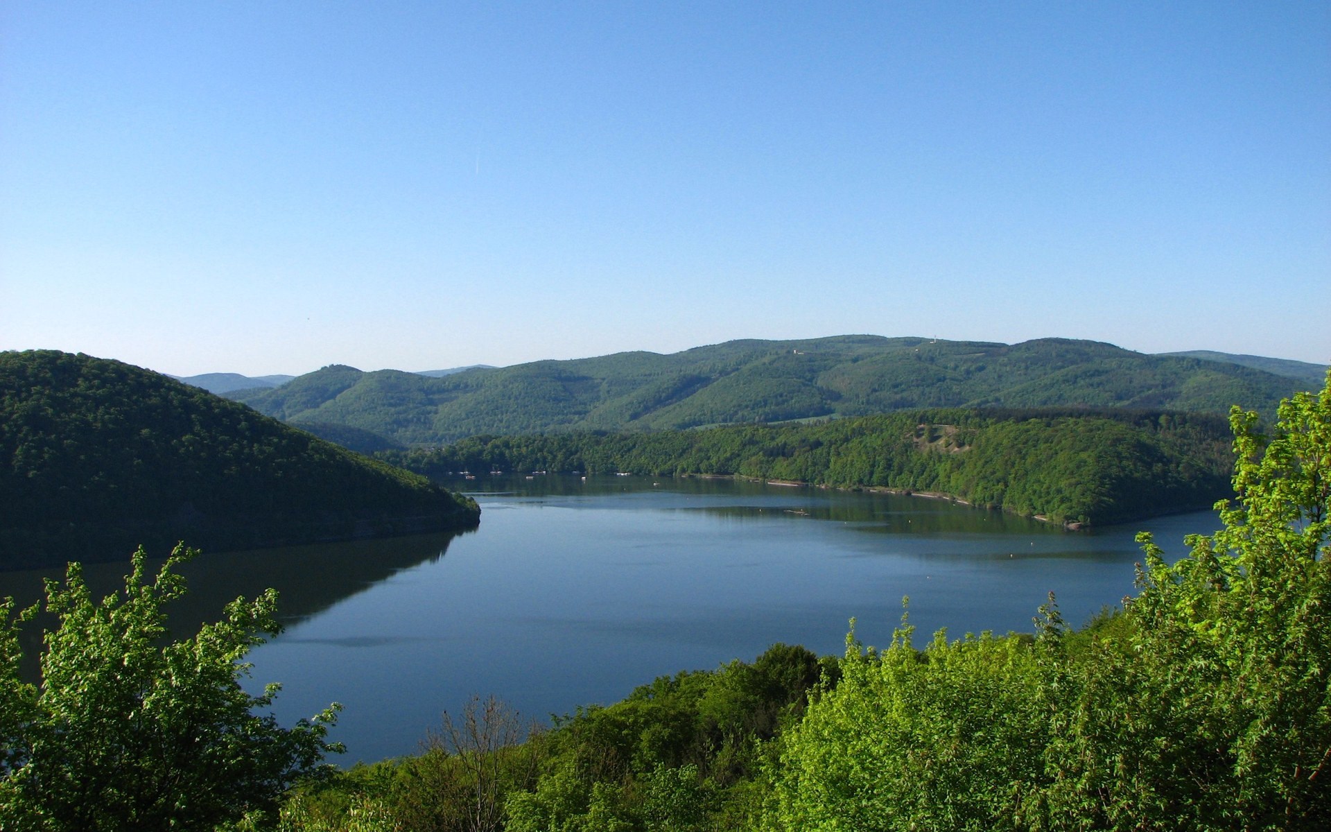 Lake surrounded by green hills under a clear blue sky HD Wallpaper