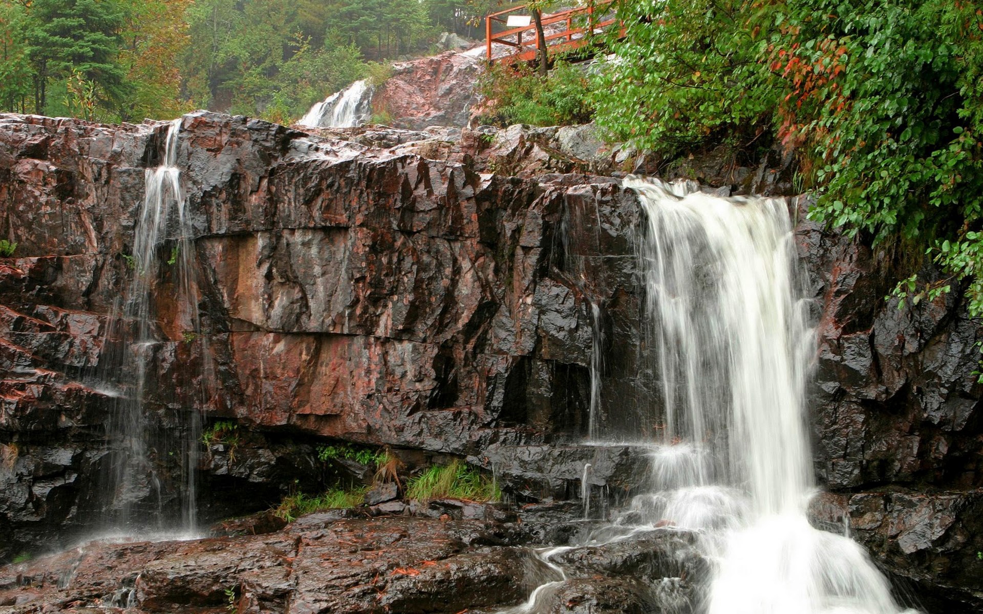 Waterfall cascading over rocky cliffs with lush greenery HD Wallpaper