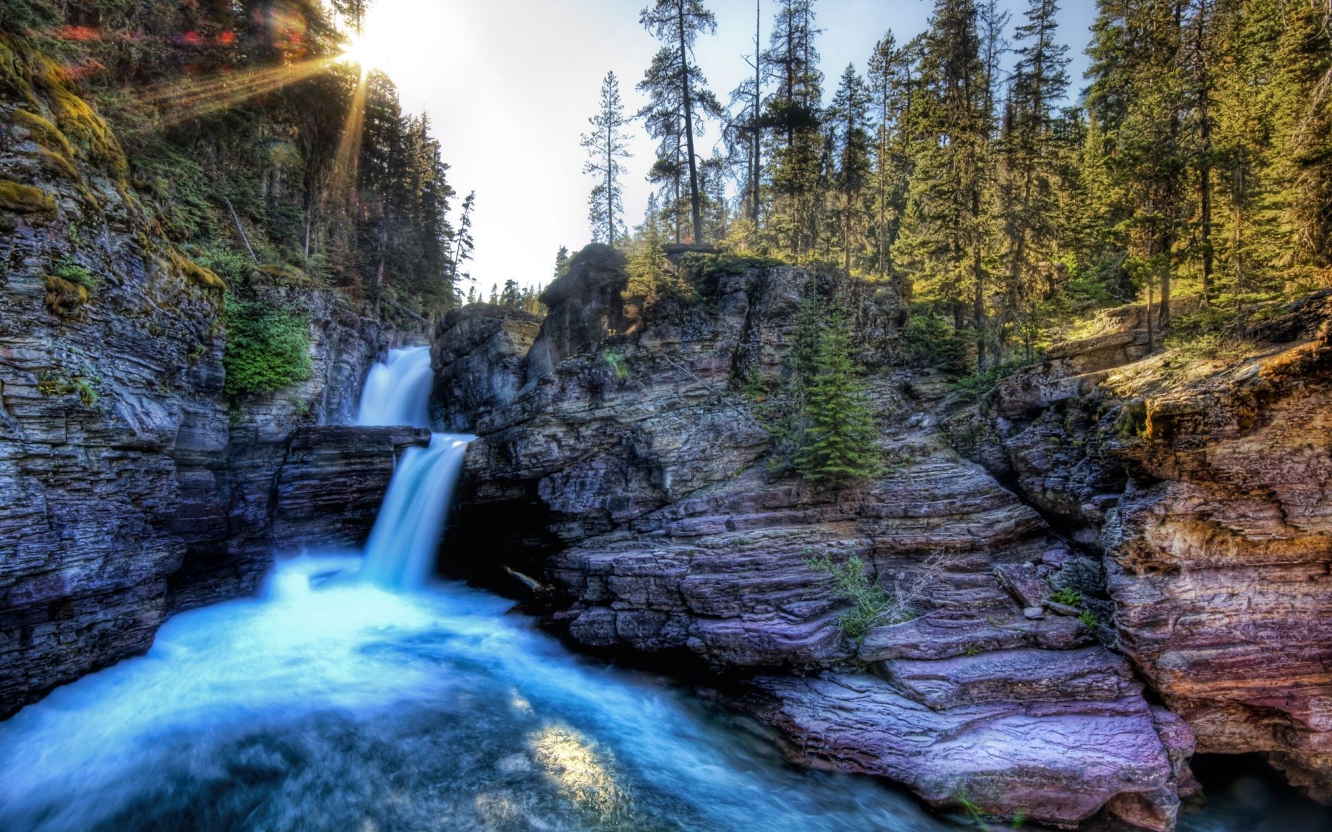 Waterfall cascading over rocky cliffs in a forest HD Wallpaper