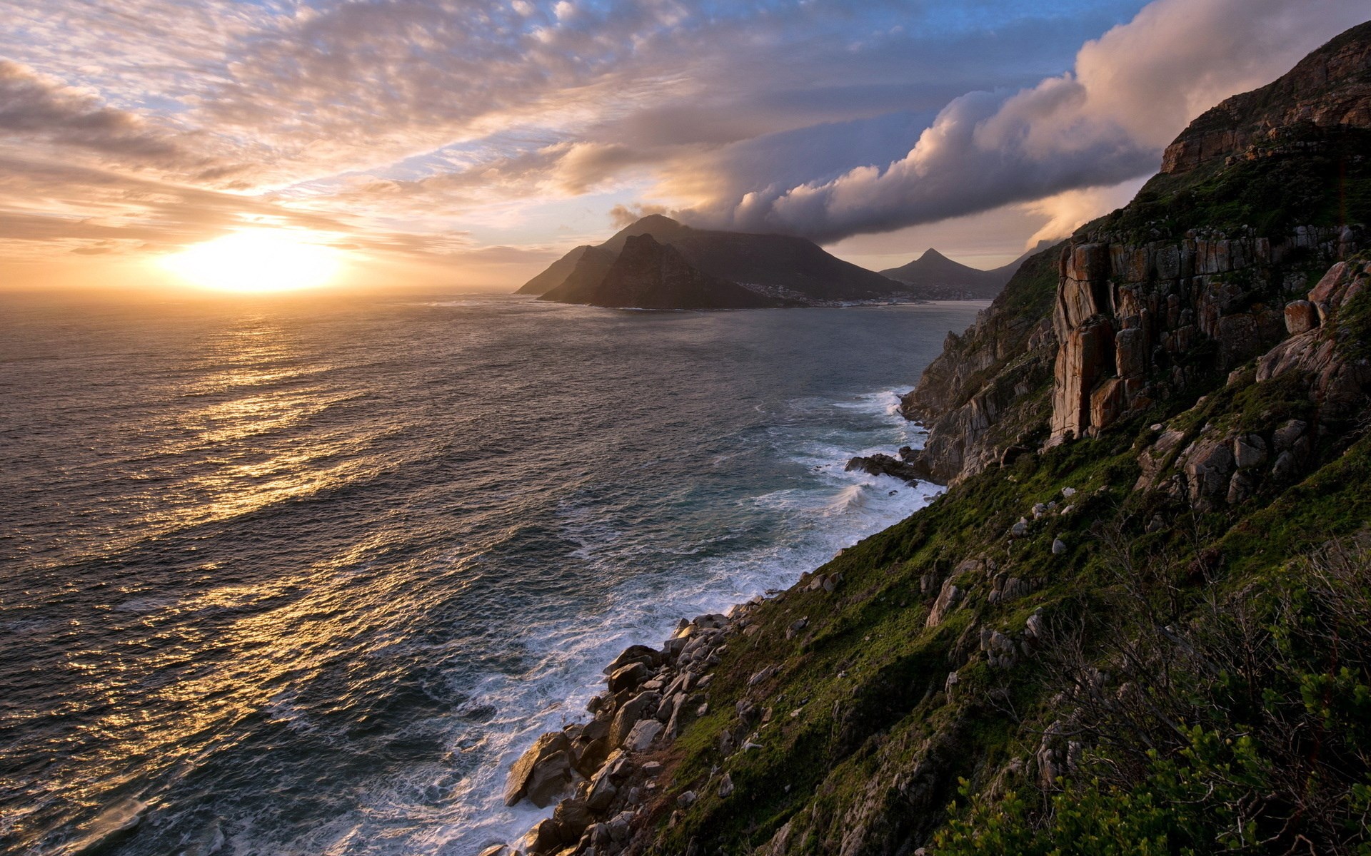 Sunset over a rocky coastline with mountains in the distance HD Wallpaper
